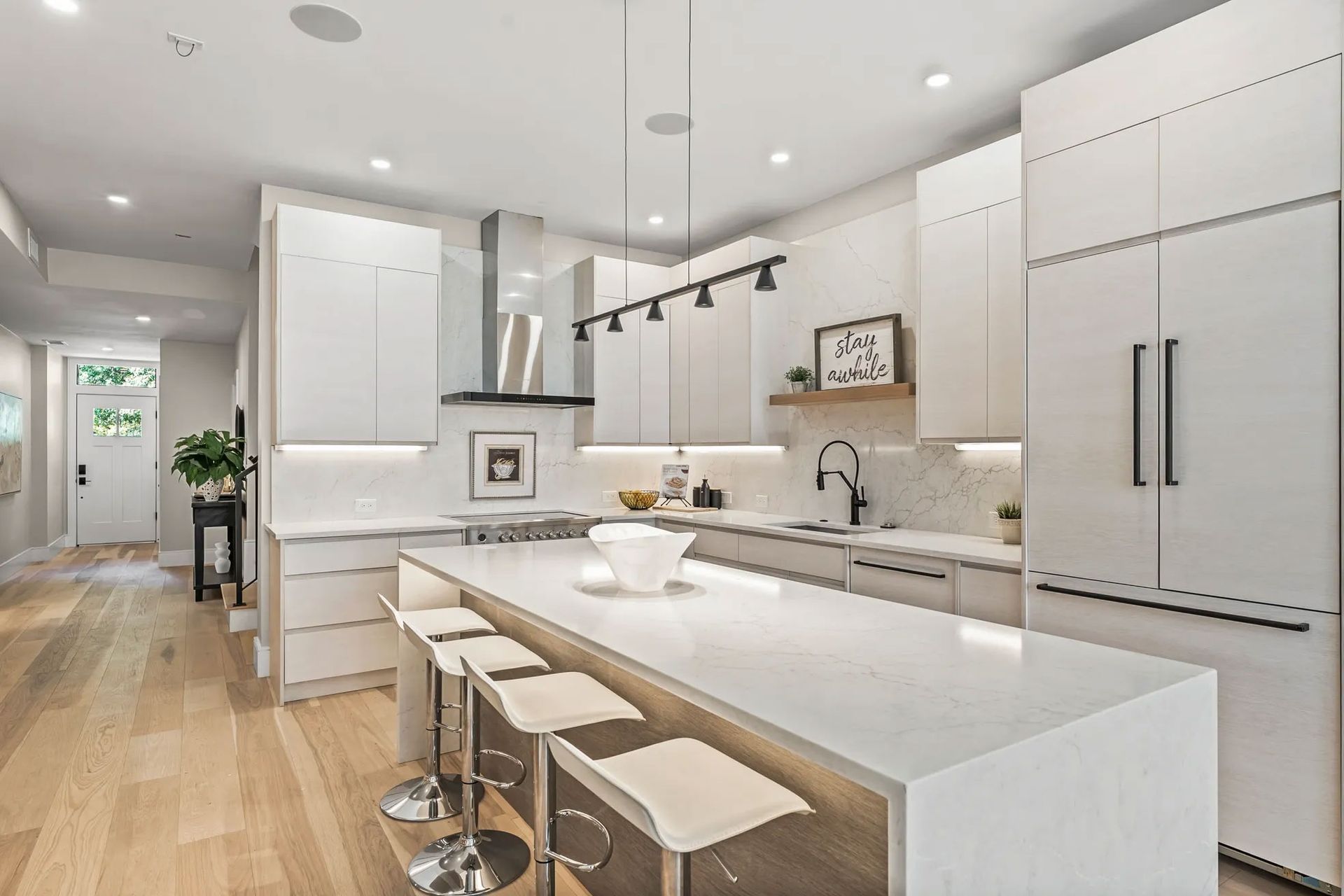 Modern white kitchen with island, seating, and stainless steel appliances.