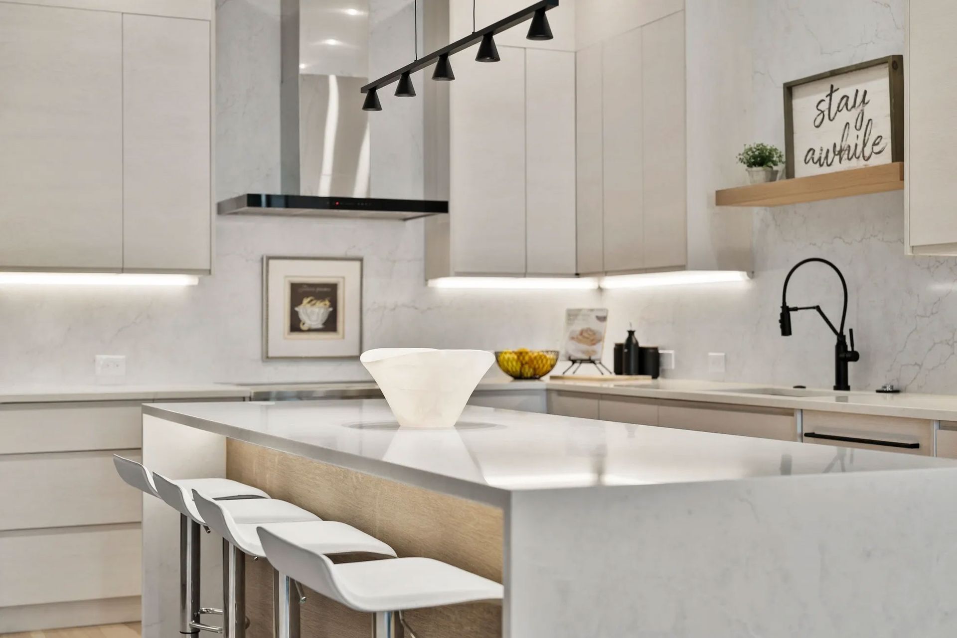 Modern white kitchen with island seating, track lighting, and decor.
