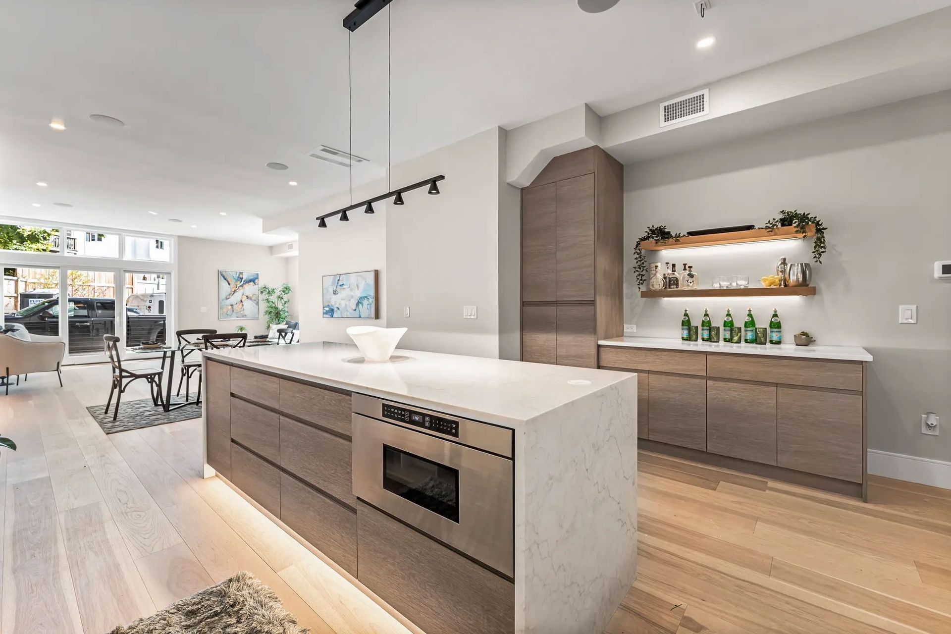Modern kitchen with island, wooden cabinets, and bar area, bathed in natural light from a window.