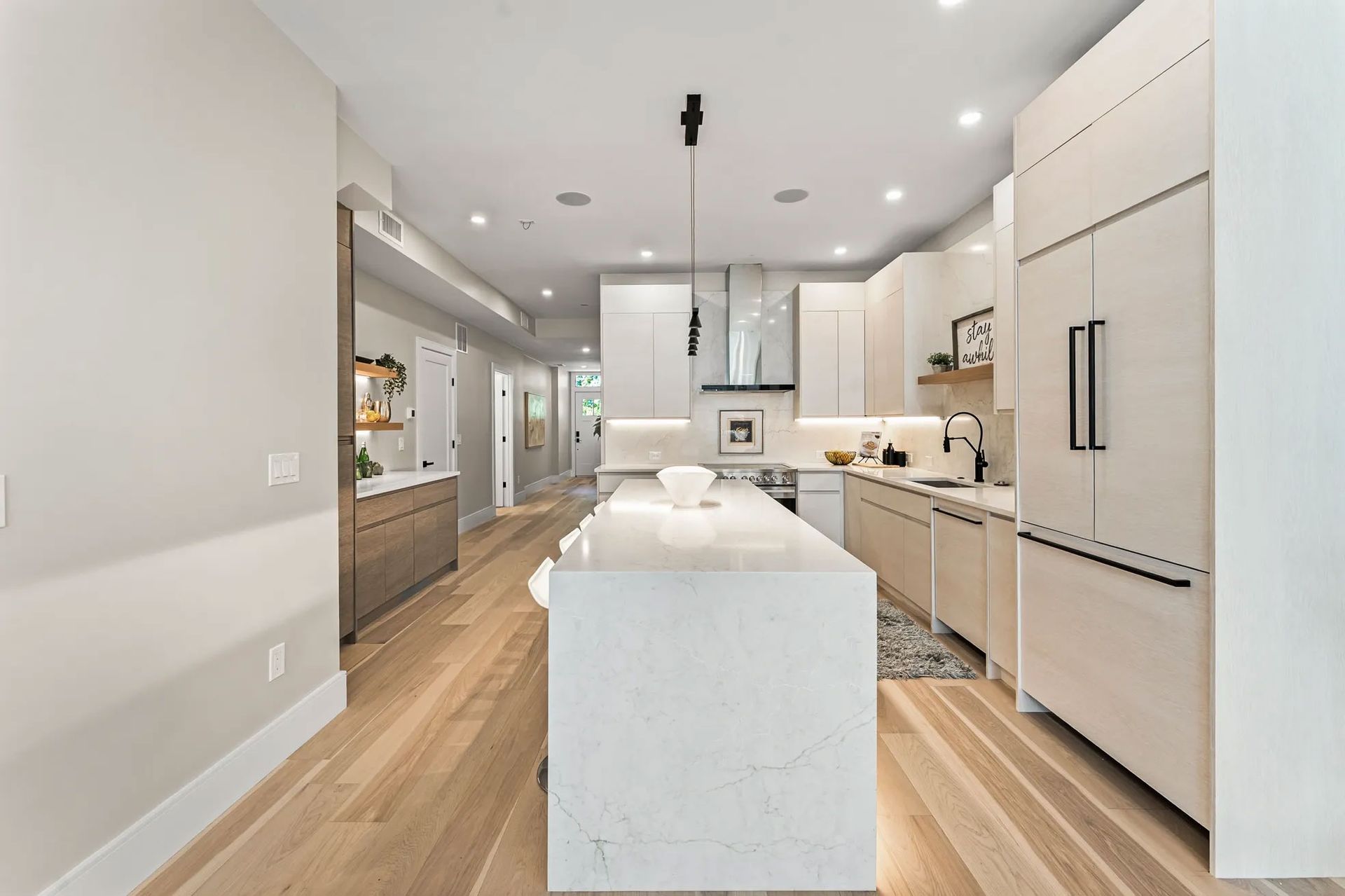 Modern white kitchen with a large island, wood floors, and recessed lighting.