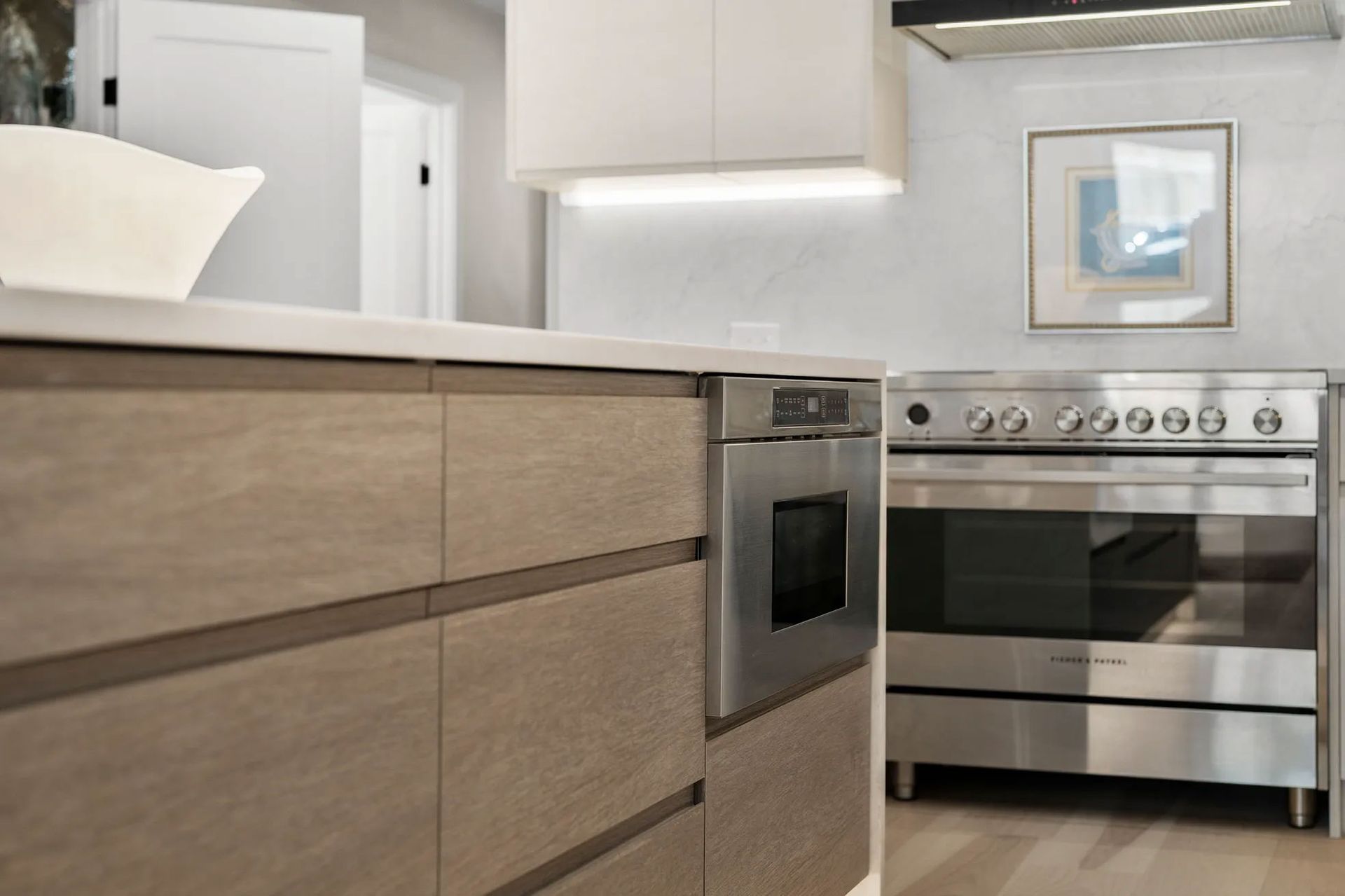 Modern kitchen with wood cabinets, stainless steel oven, and white countertops.