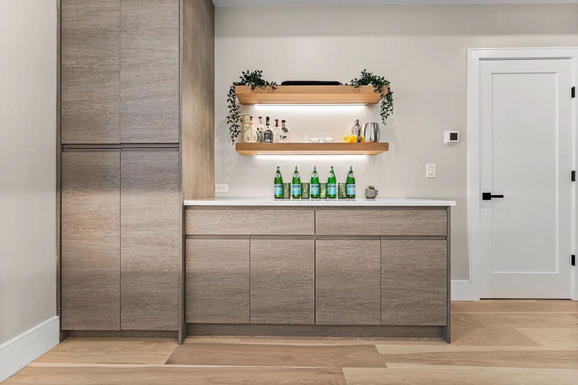 Modern home bar with gray cabinetry, white countertop, open shelving, and beer bottles.