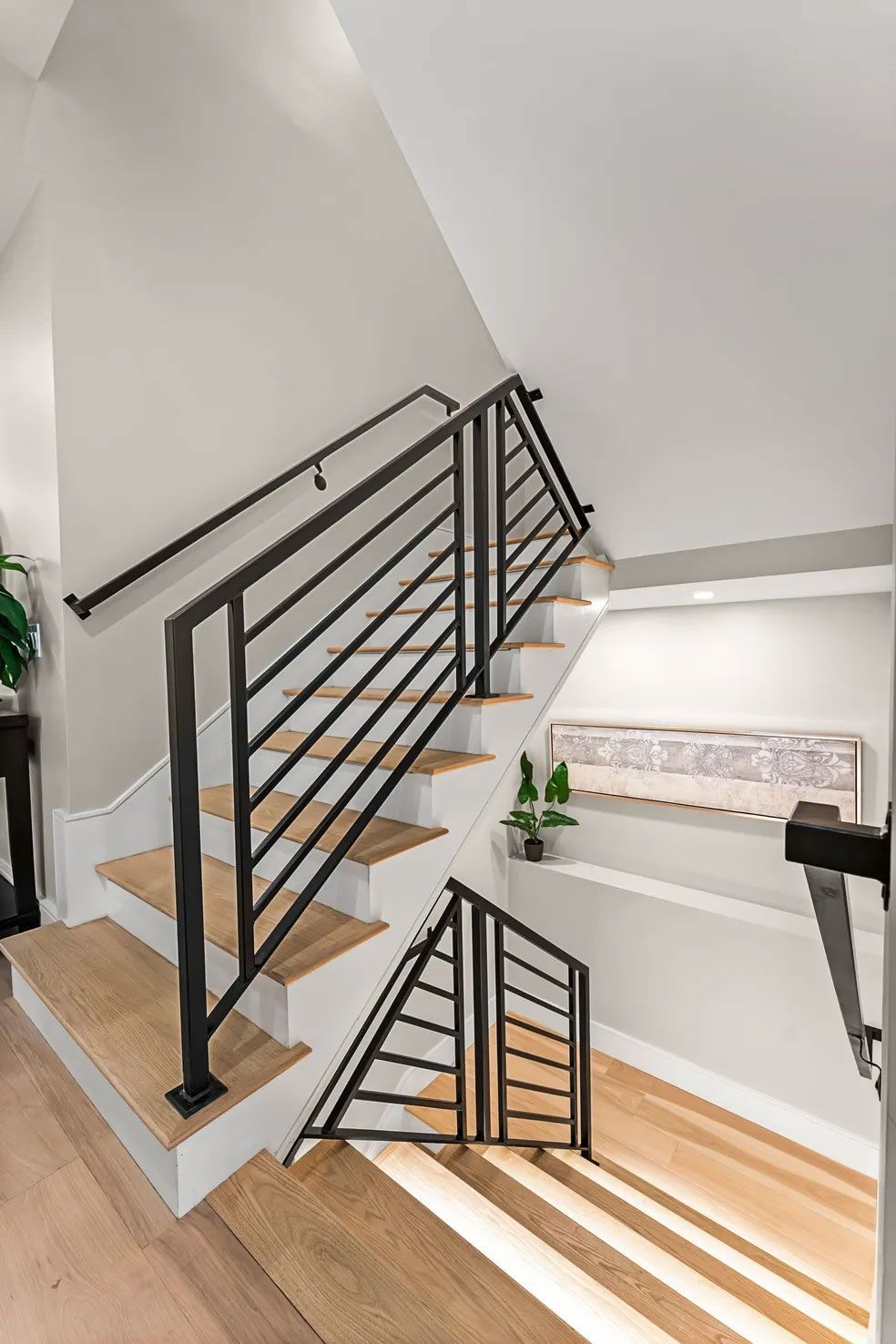 Staircase with light wood steps, white risers, black metal railings, and light walls.