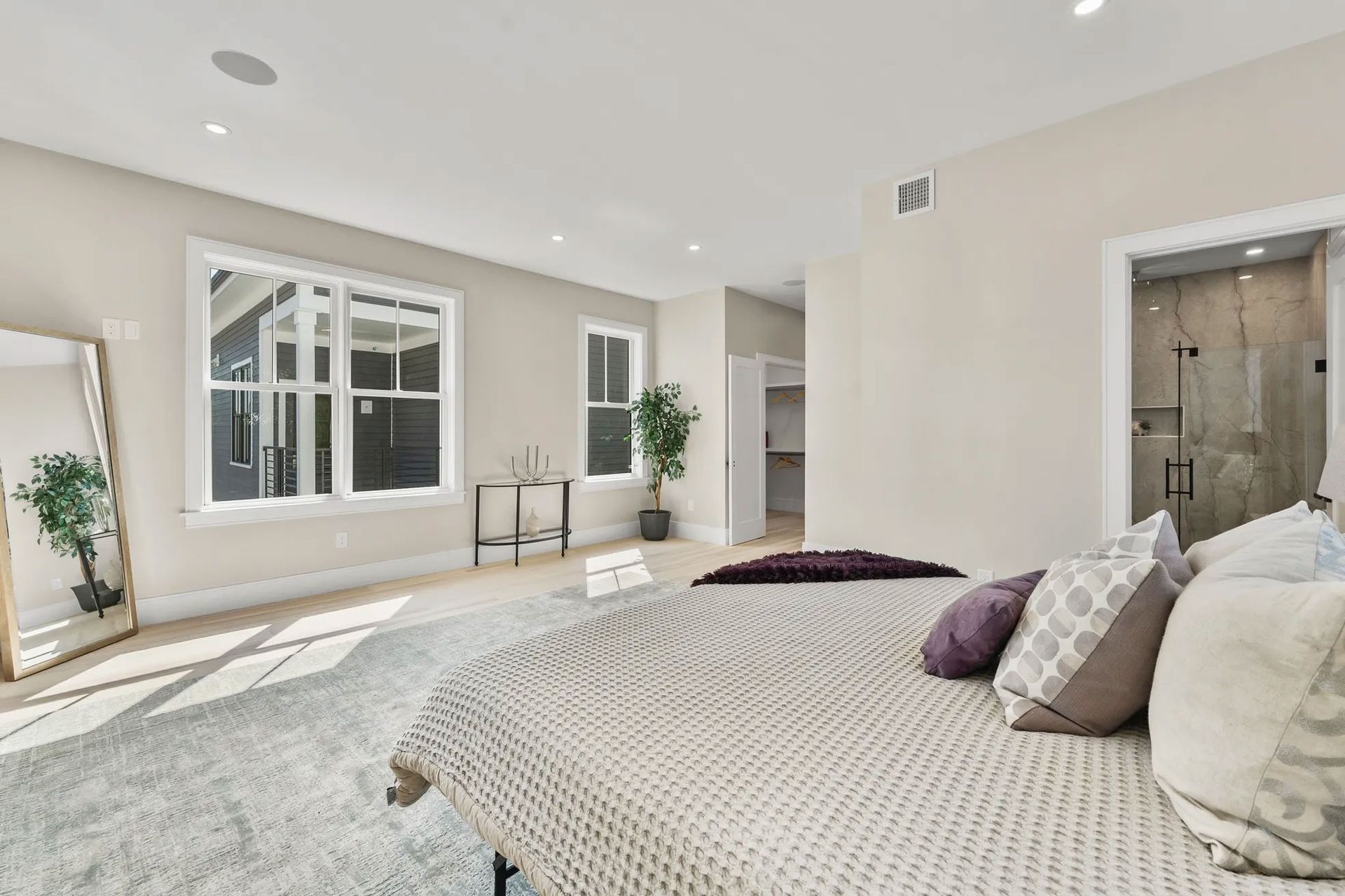 Spacious bedroom with a large bed, full-length mirror, windows, and an en-suite bathroom.