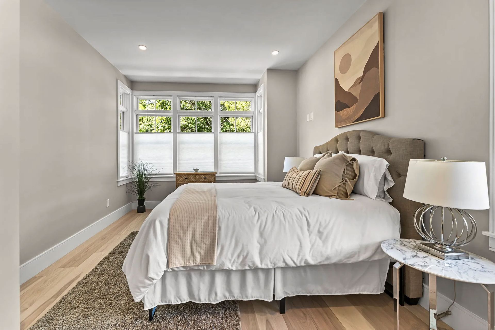 Bedroom with bed, rug, window, neutral walls, art, and side table.