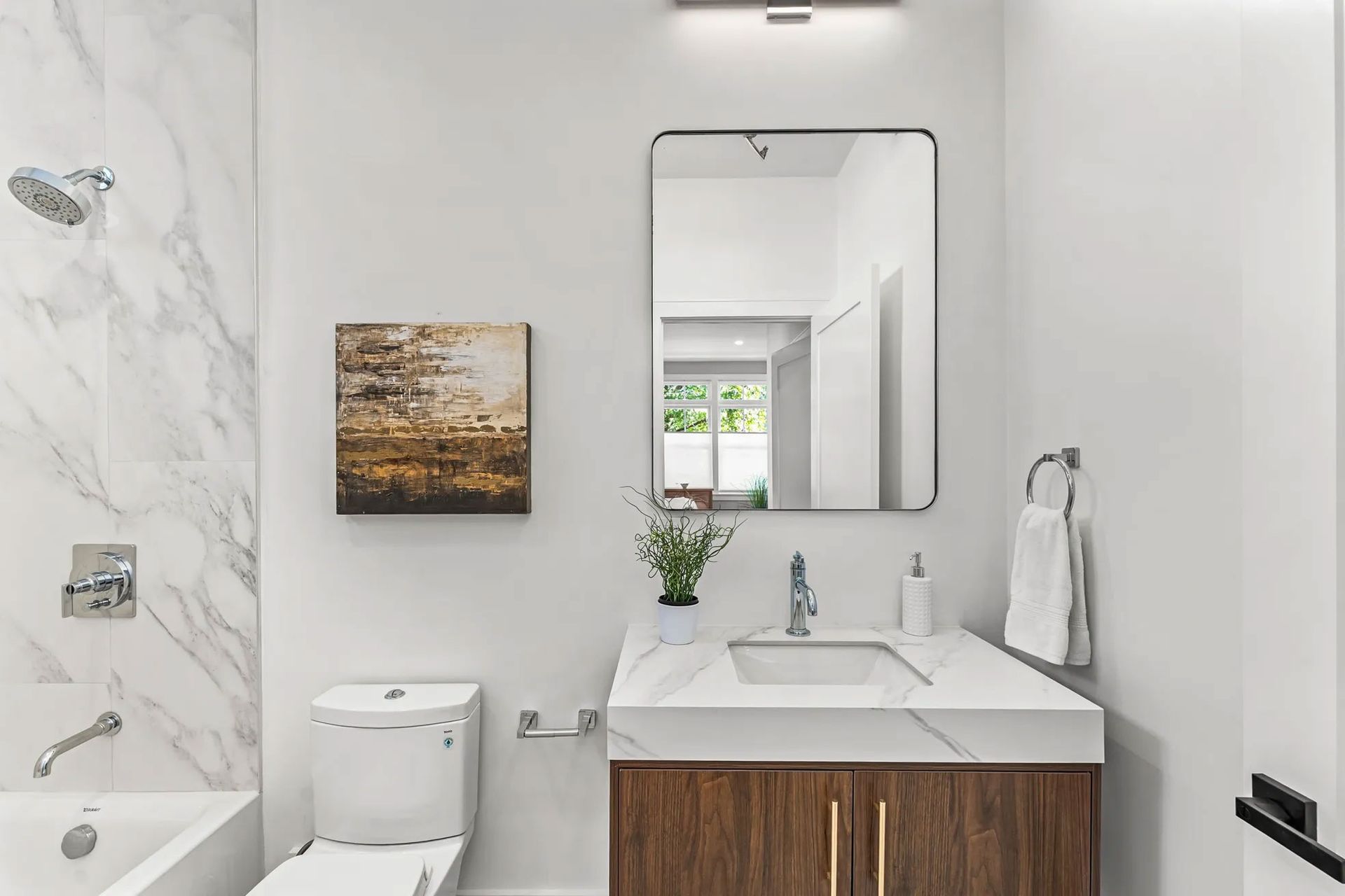 Bathroom with white marble tile, wood vanity, and a framed mirror.