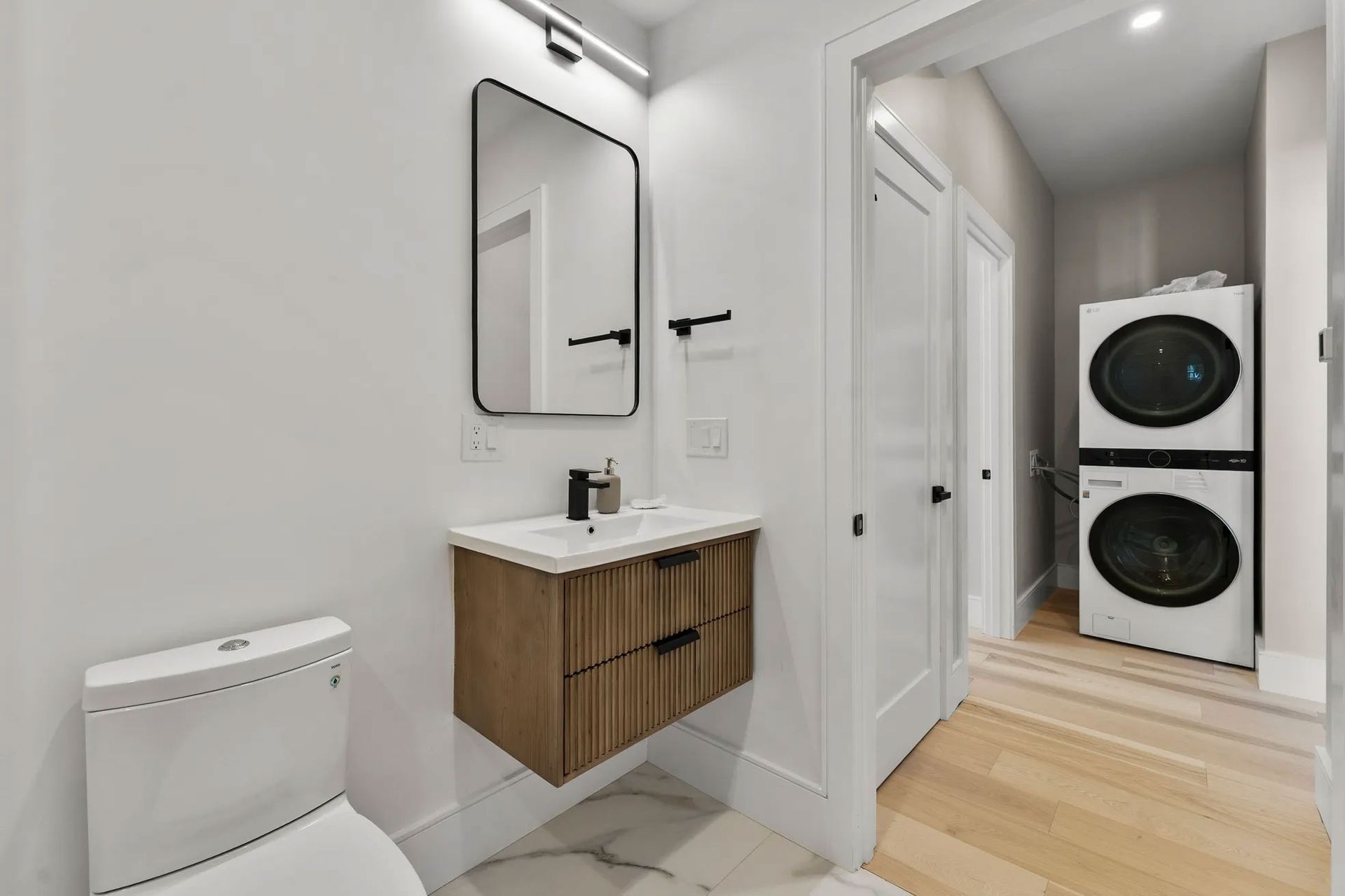 Bathroom with a floating wood vanity, black mirror, and stacked washer/dryer in a separate alcove.