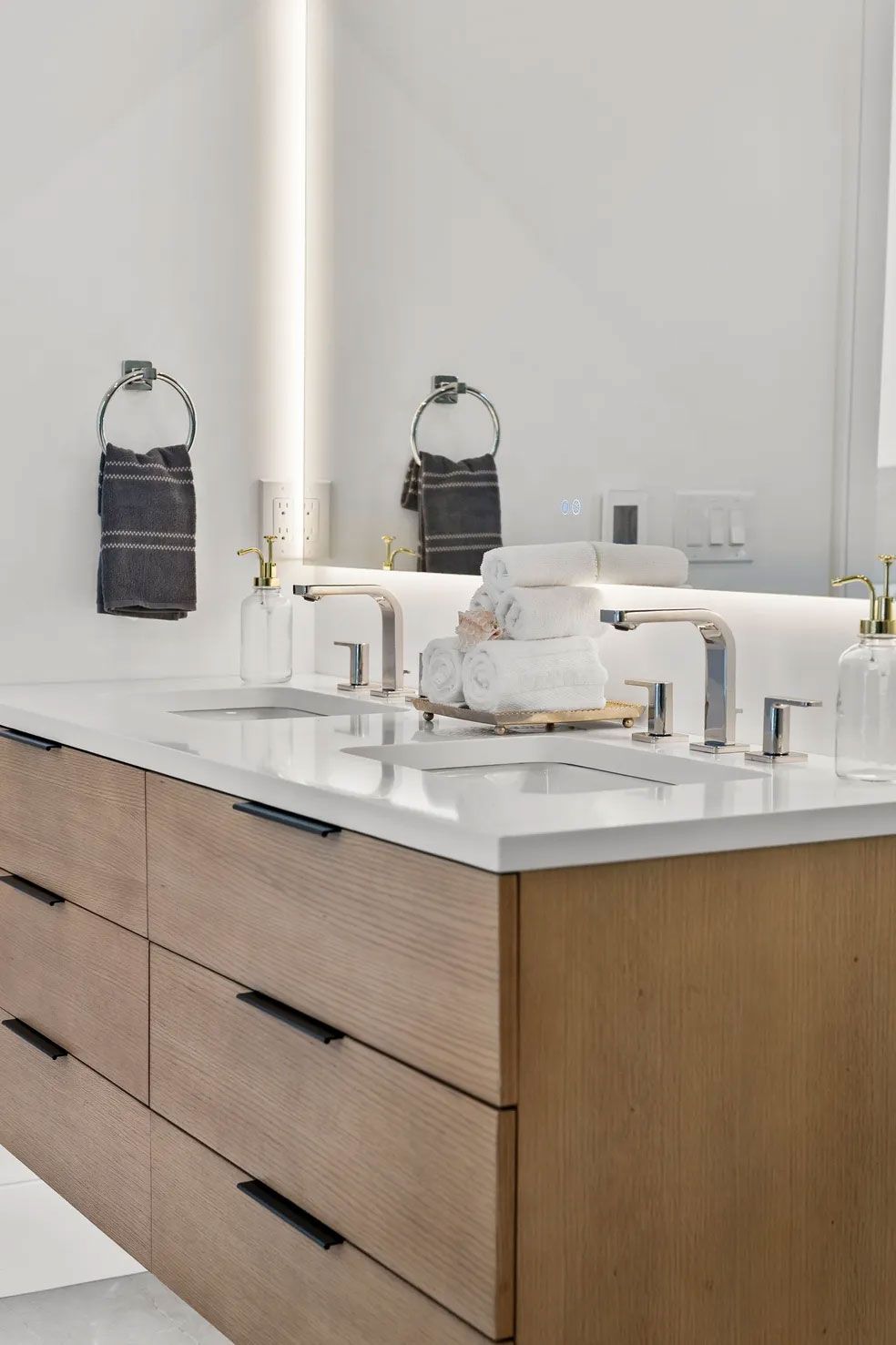 Modern bathroom with light wood vanity, white countertop, and two sinks.