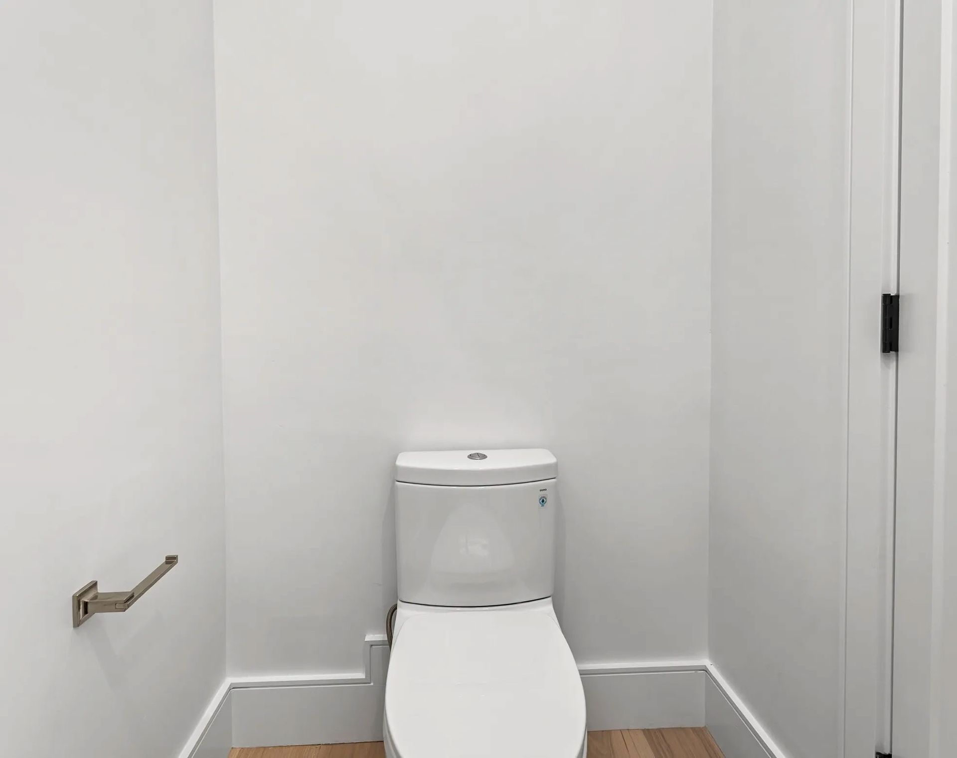 White toilet in a small white bathroom with a toilet paper holder.