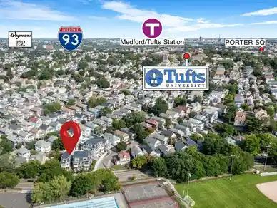 Aerial view of residential area with a red location marker. Includes highway, subway station, and Tufts University.