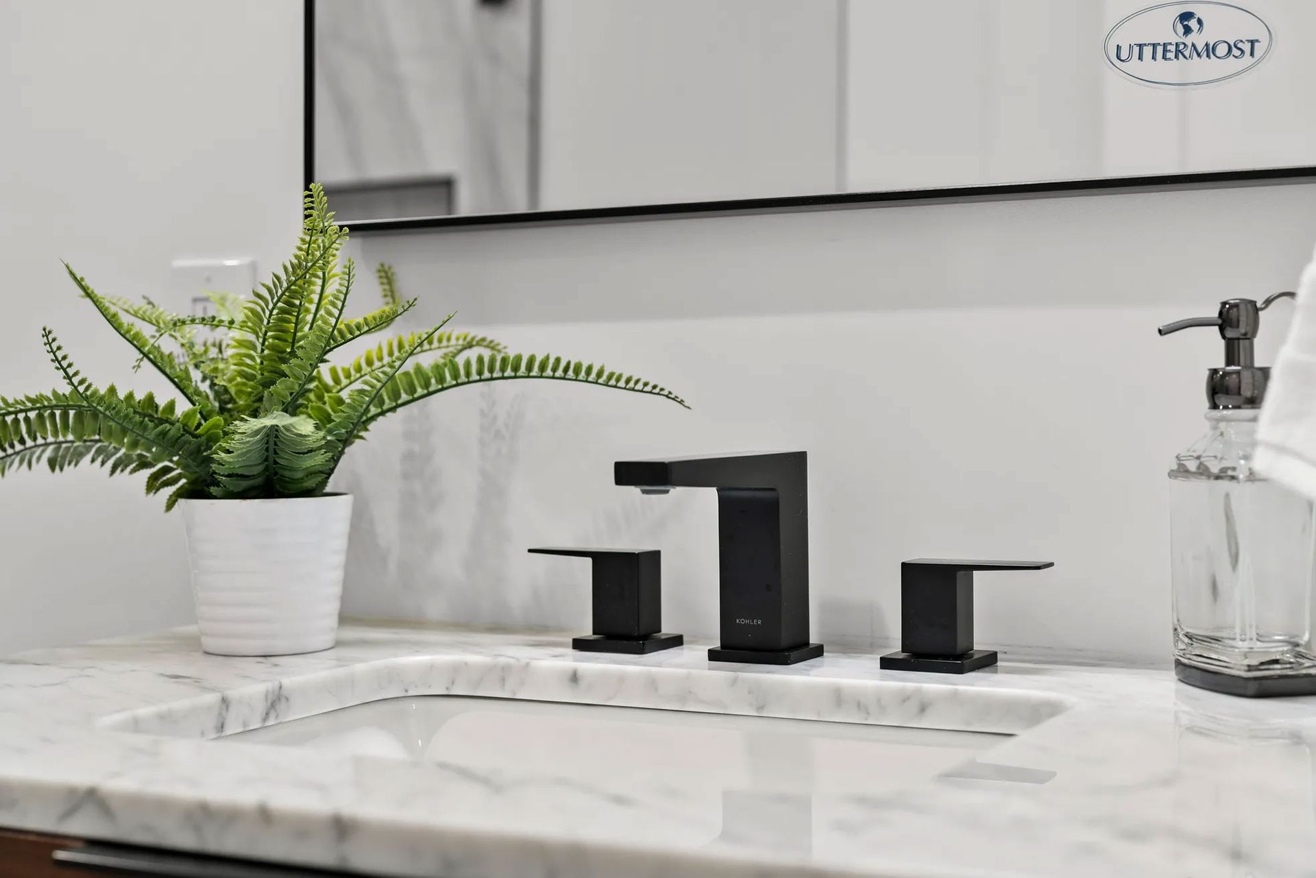 Black faucet and marble countertop with a potted fern in a bathroom.