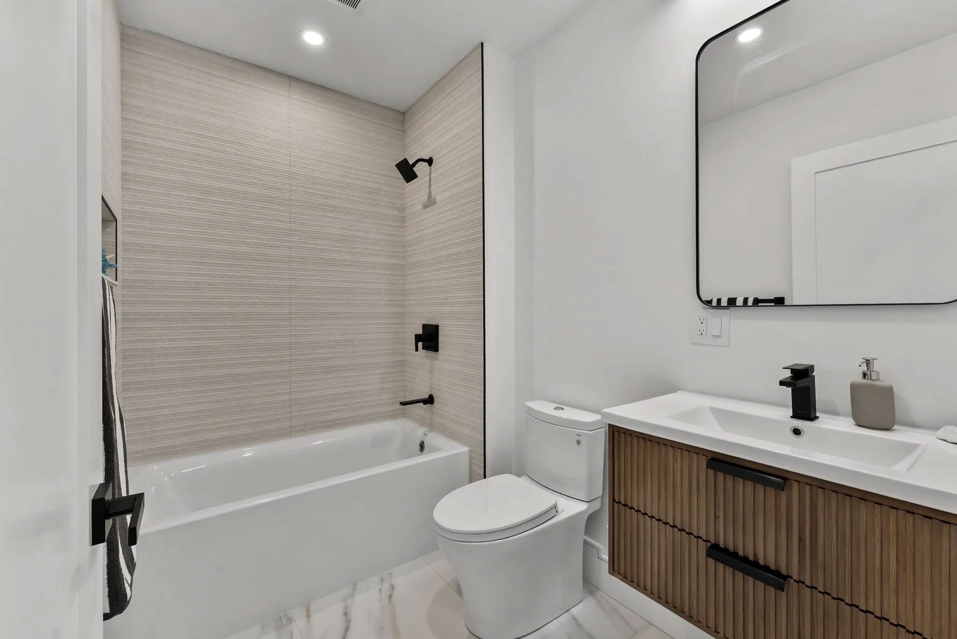 Modern bathroom with white and wood accents, features a tub, toilet, and vanity.
