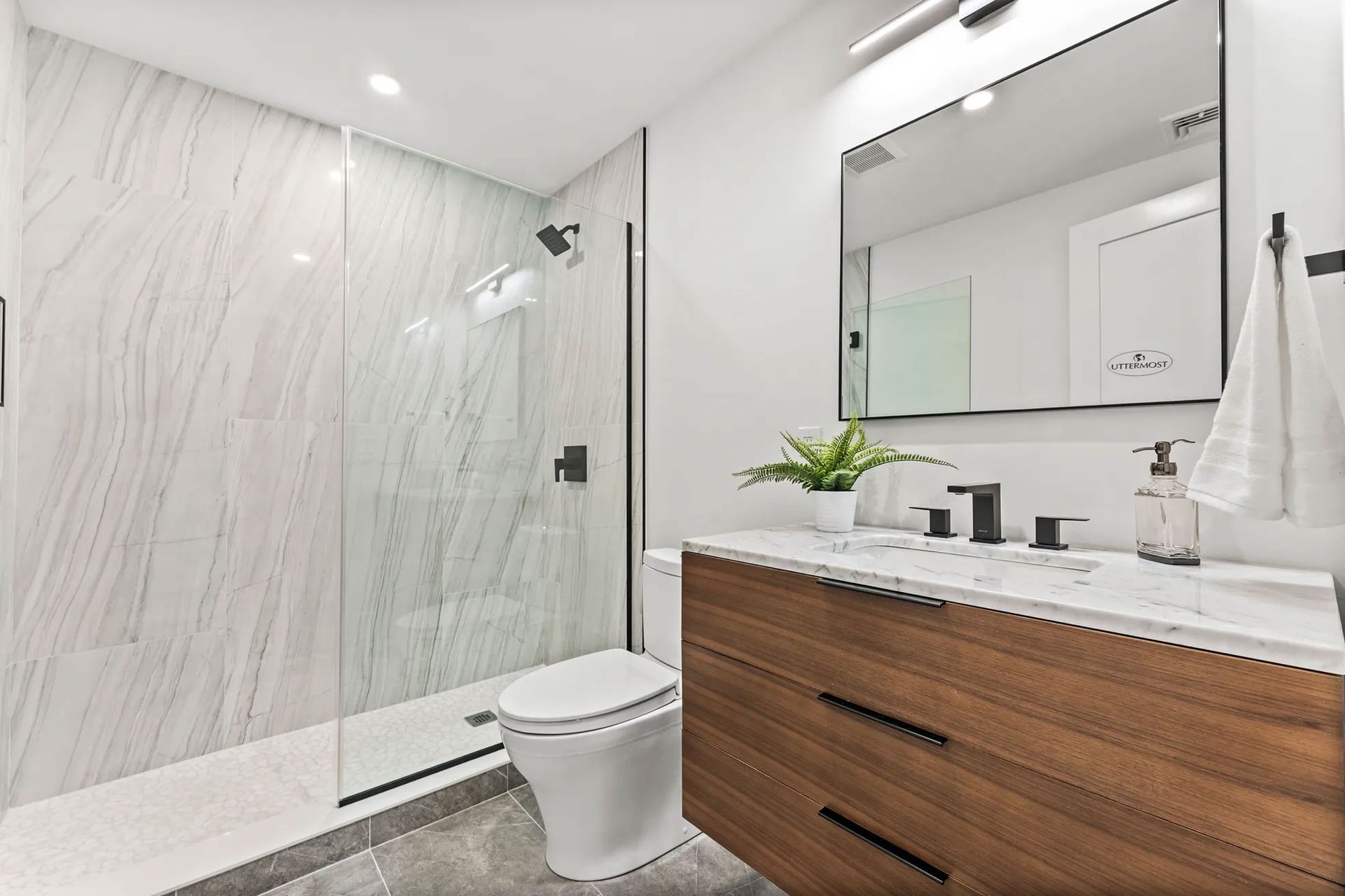 Modern bathroom with marble shower, wooden vanity, and large mirror.