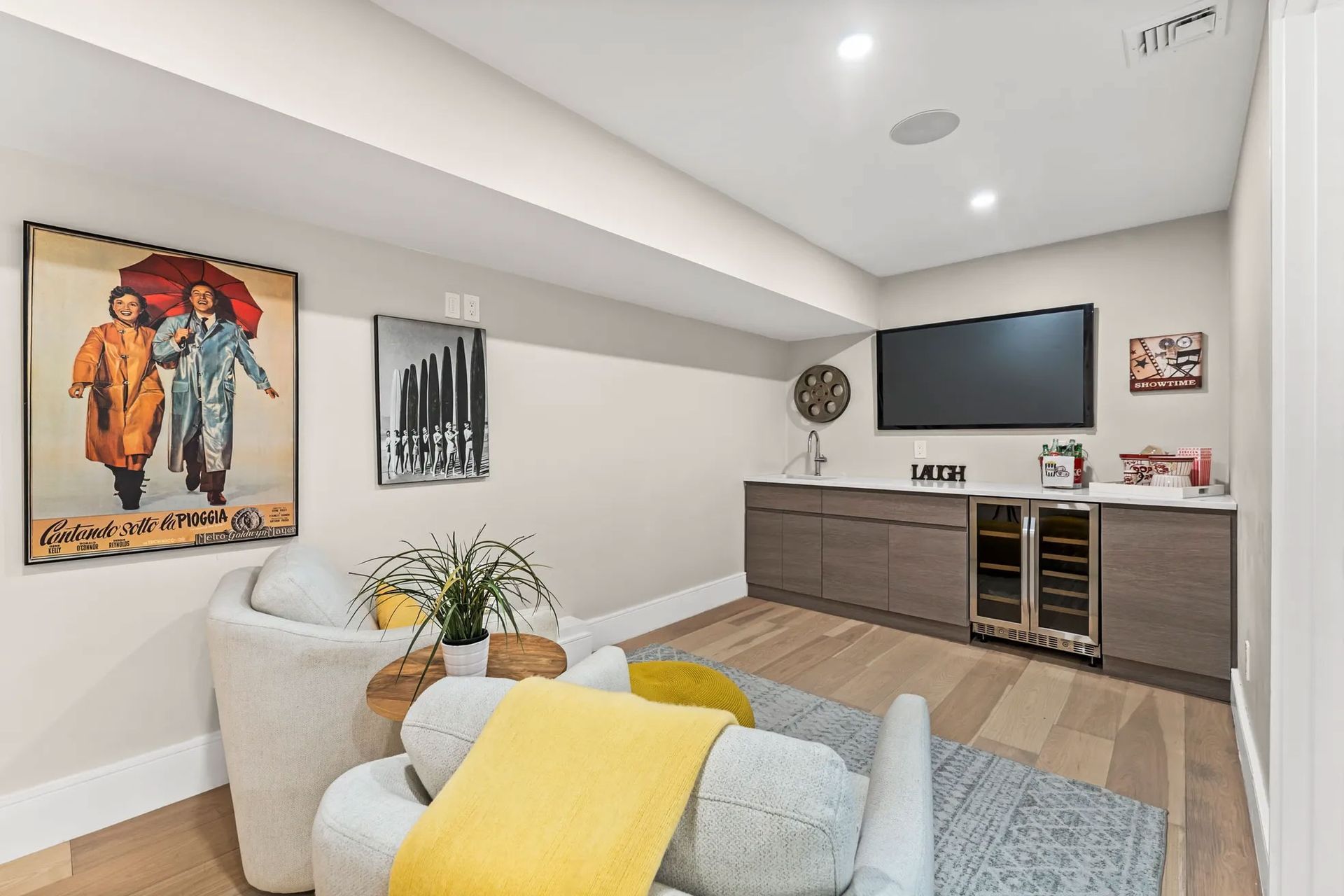 Cozy basement media room with TV, bar, seating, art, and light wood floor.