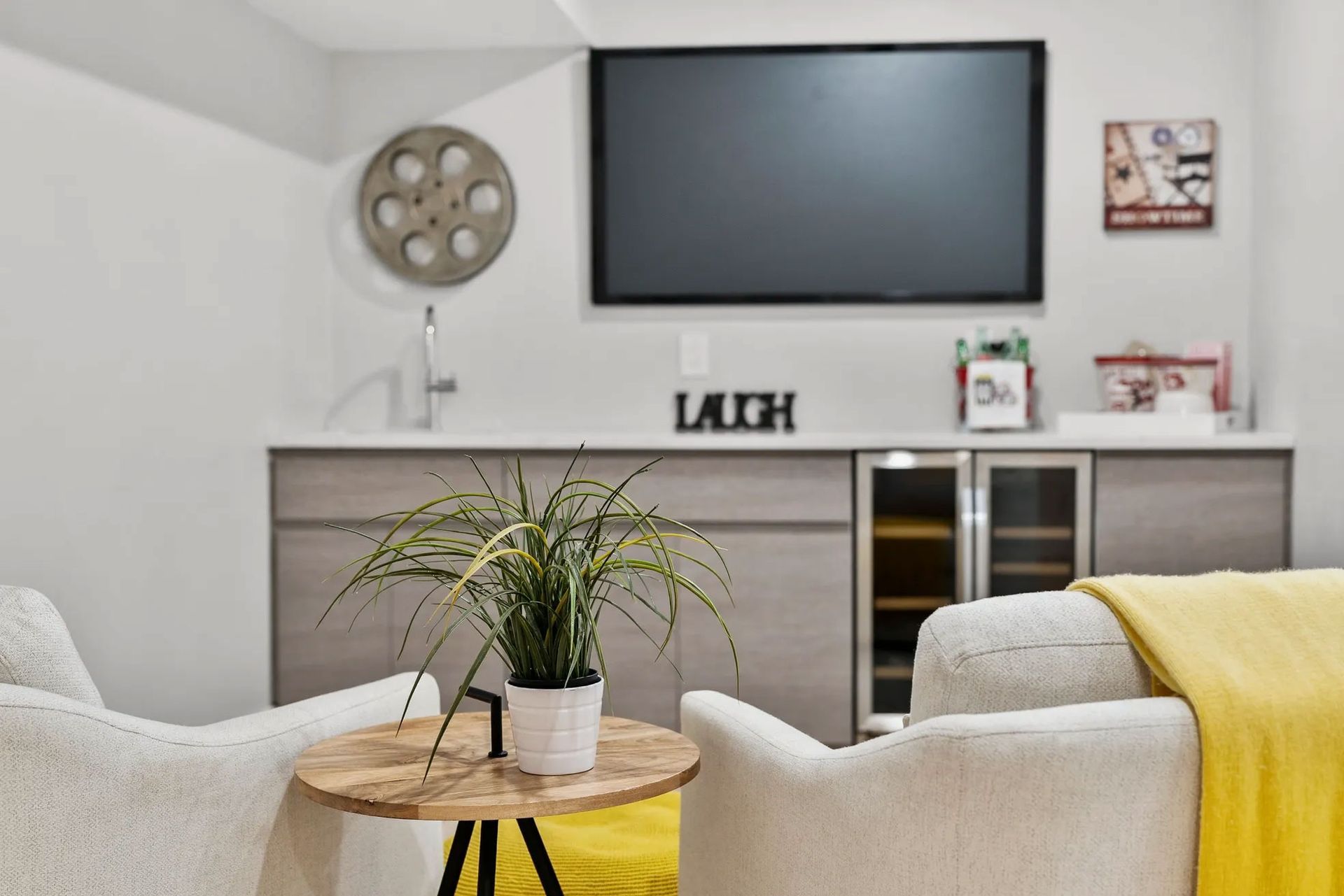 Cozy home theater with two white armchairs, TV, built-in bar, and decor.