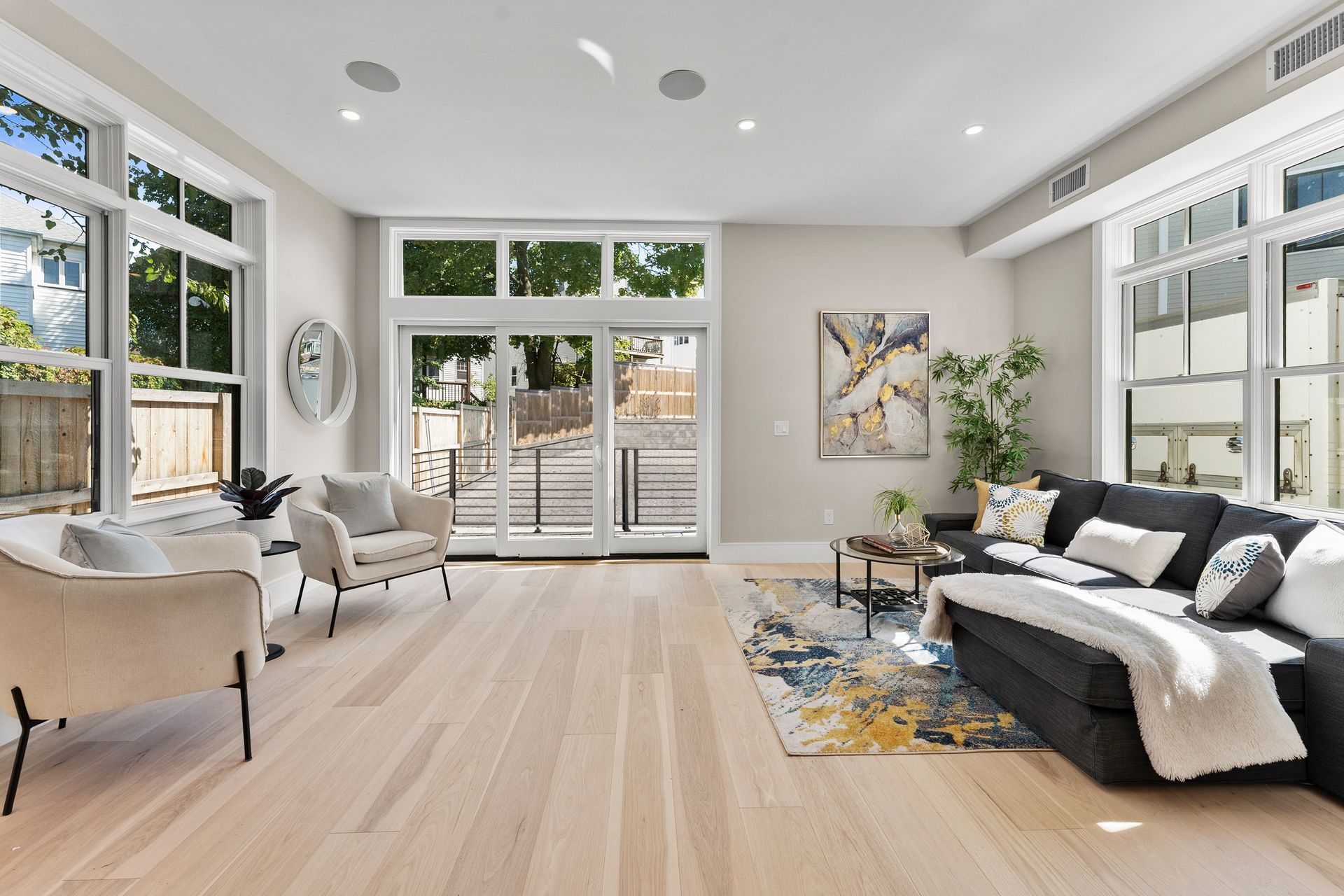 Bright, modern living room with light wood floors, large windows, and a dark gray sectional sofa.