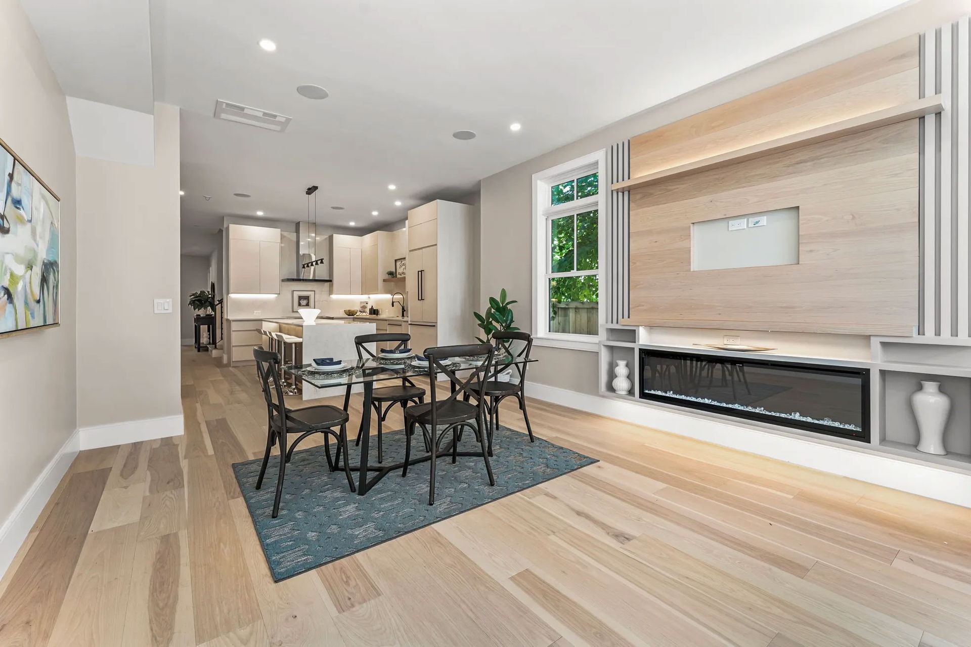 Open-concept dining and kitchen area with light wood floors, a fireplace, and a dining table with six chairs.
