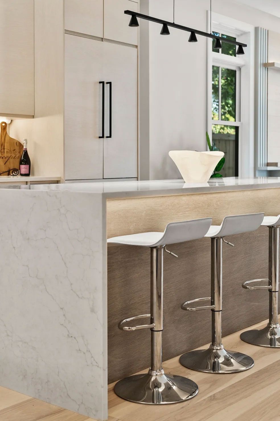 Modern kitchen with white countertops, bar stools, and a refrigerator.