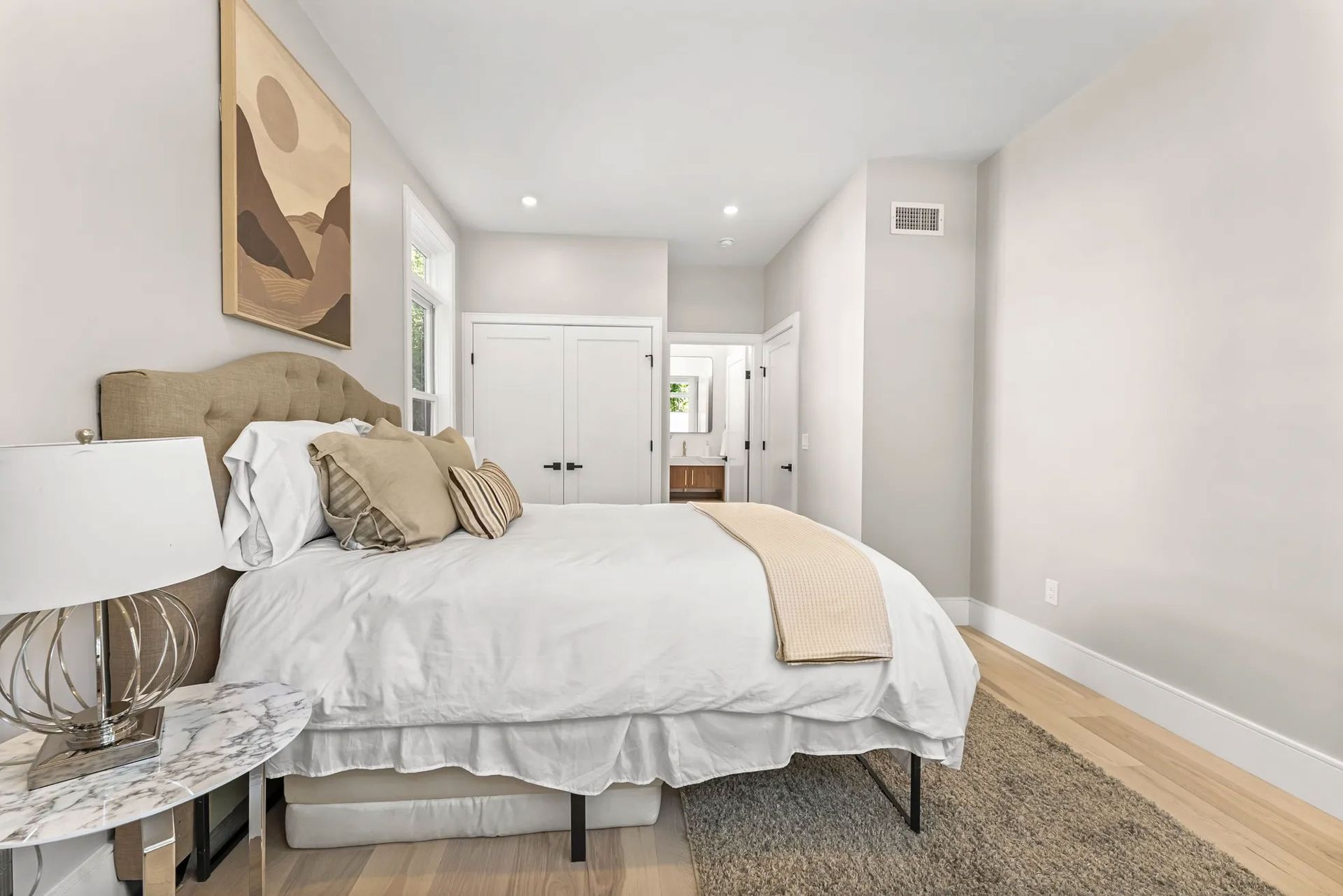 Bedroom with a bed, nightstand, artwork, closet, and a doorway to a bathroom.