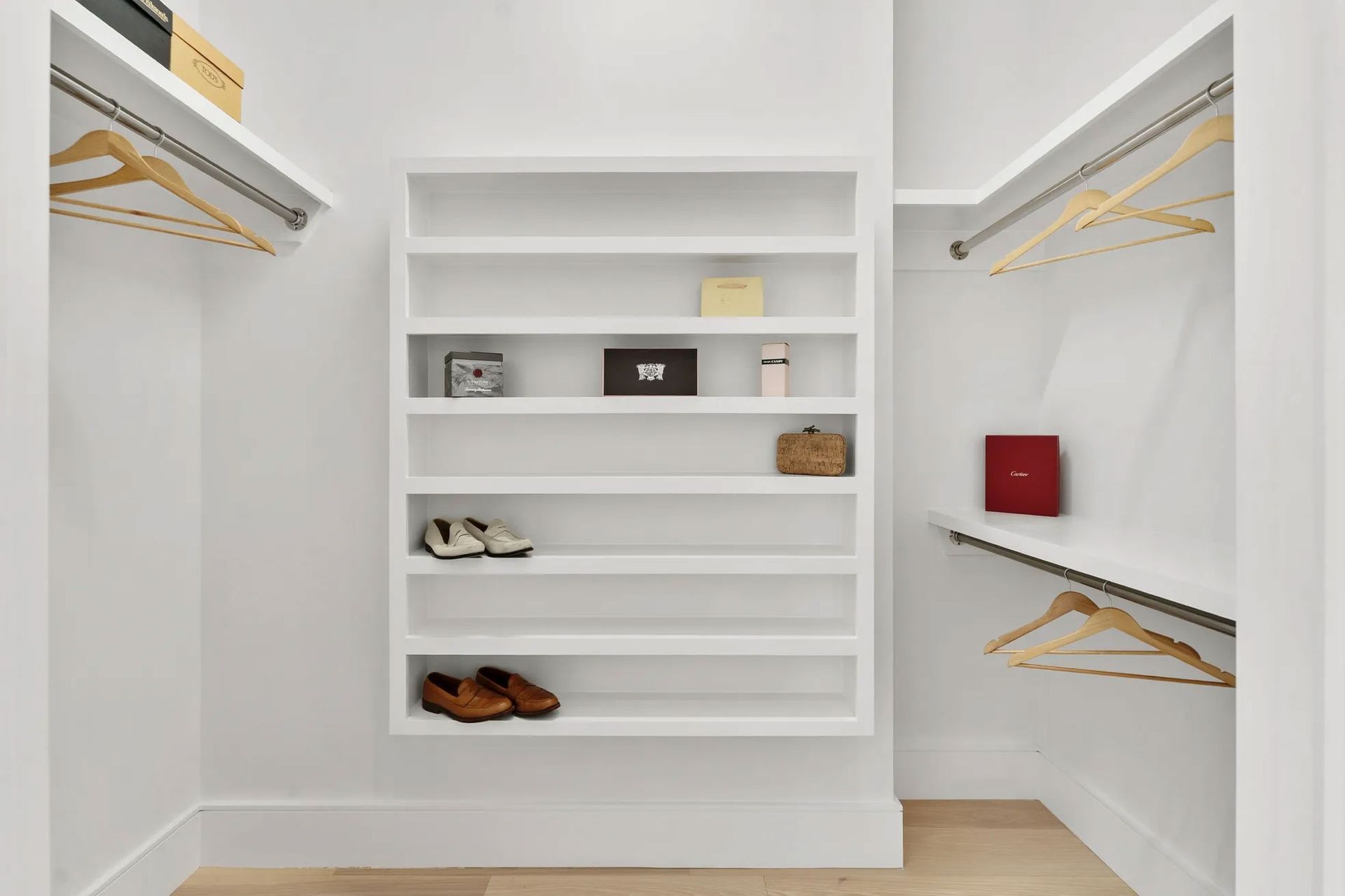 White closet with open shelving and hanging rods; items on shelves and hangers.