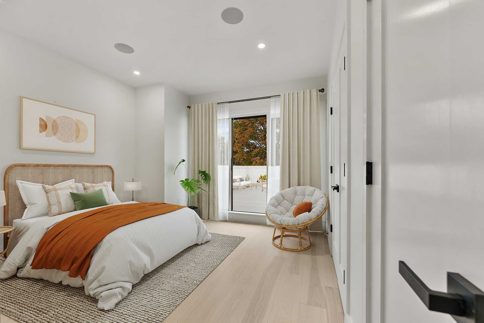 Bedroom with bed, chair, and large window; white walls, neutral tones, and sunlight.