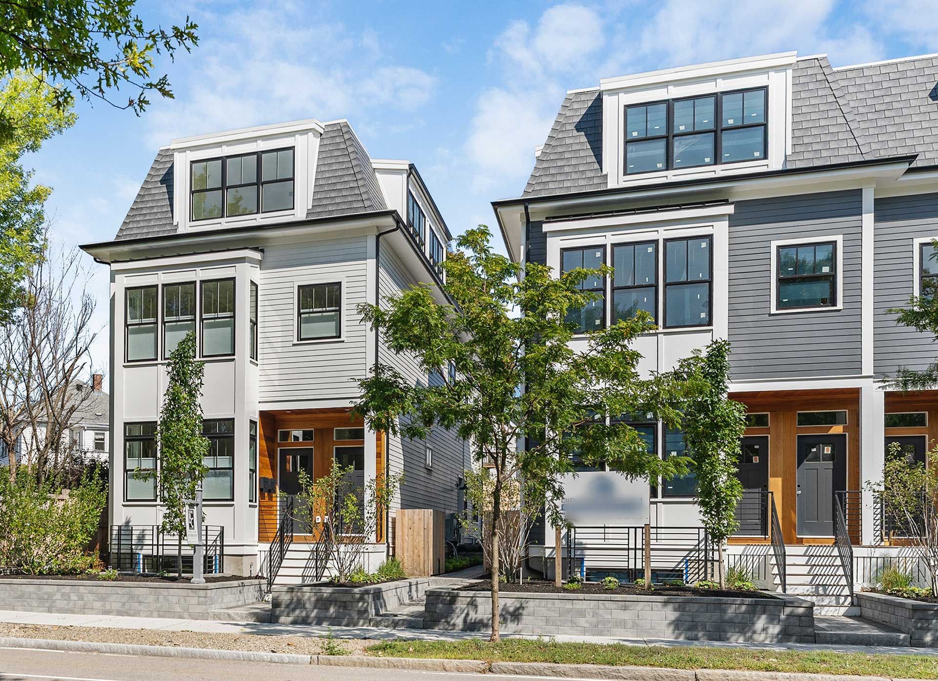 Two-story townhouses with gray and white siding, dark trim, and dormers, set behind small front yards.
