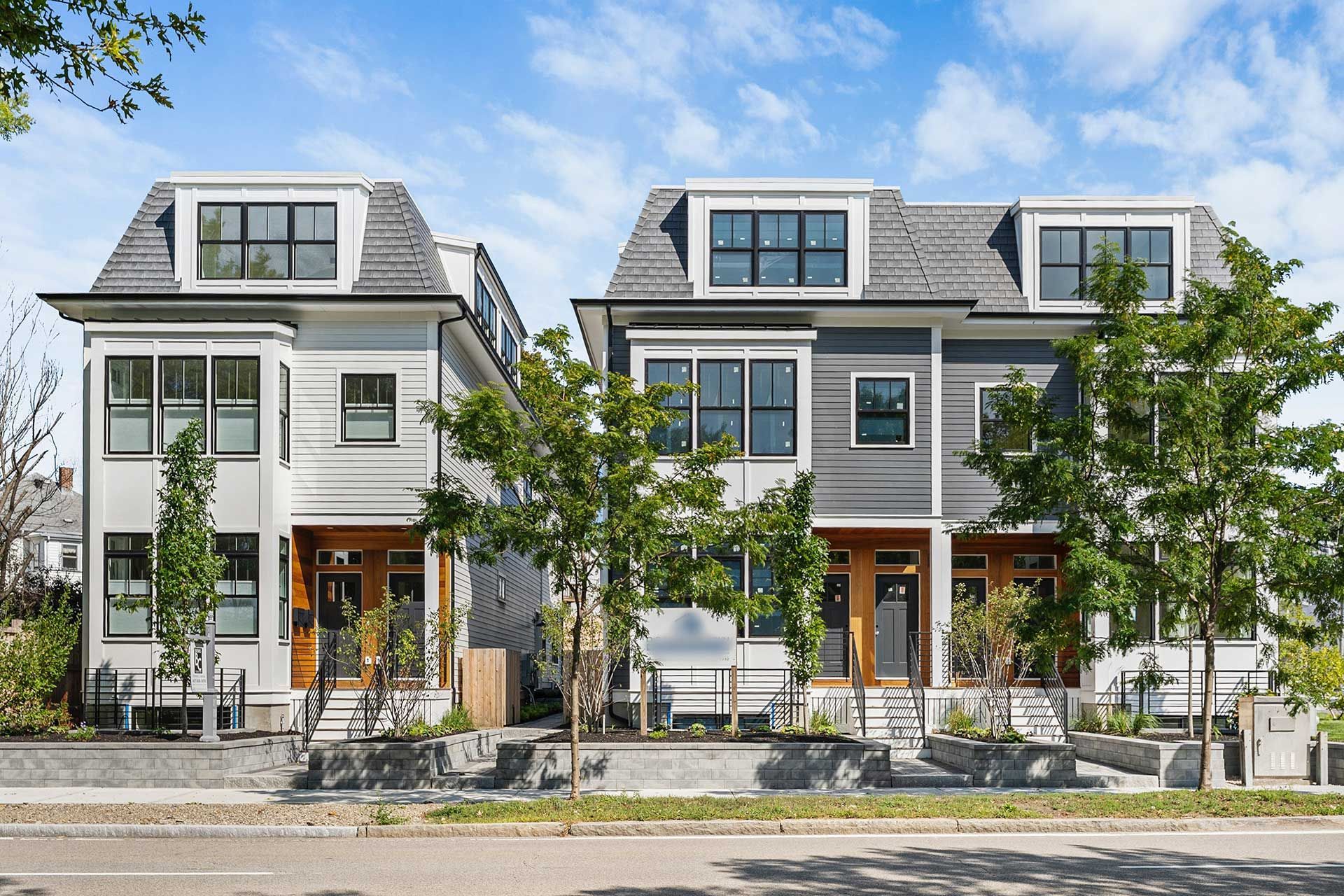 Two modern townhouses with dormers, grey siding, and front steps, under a blue sky.