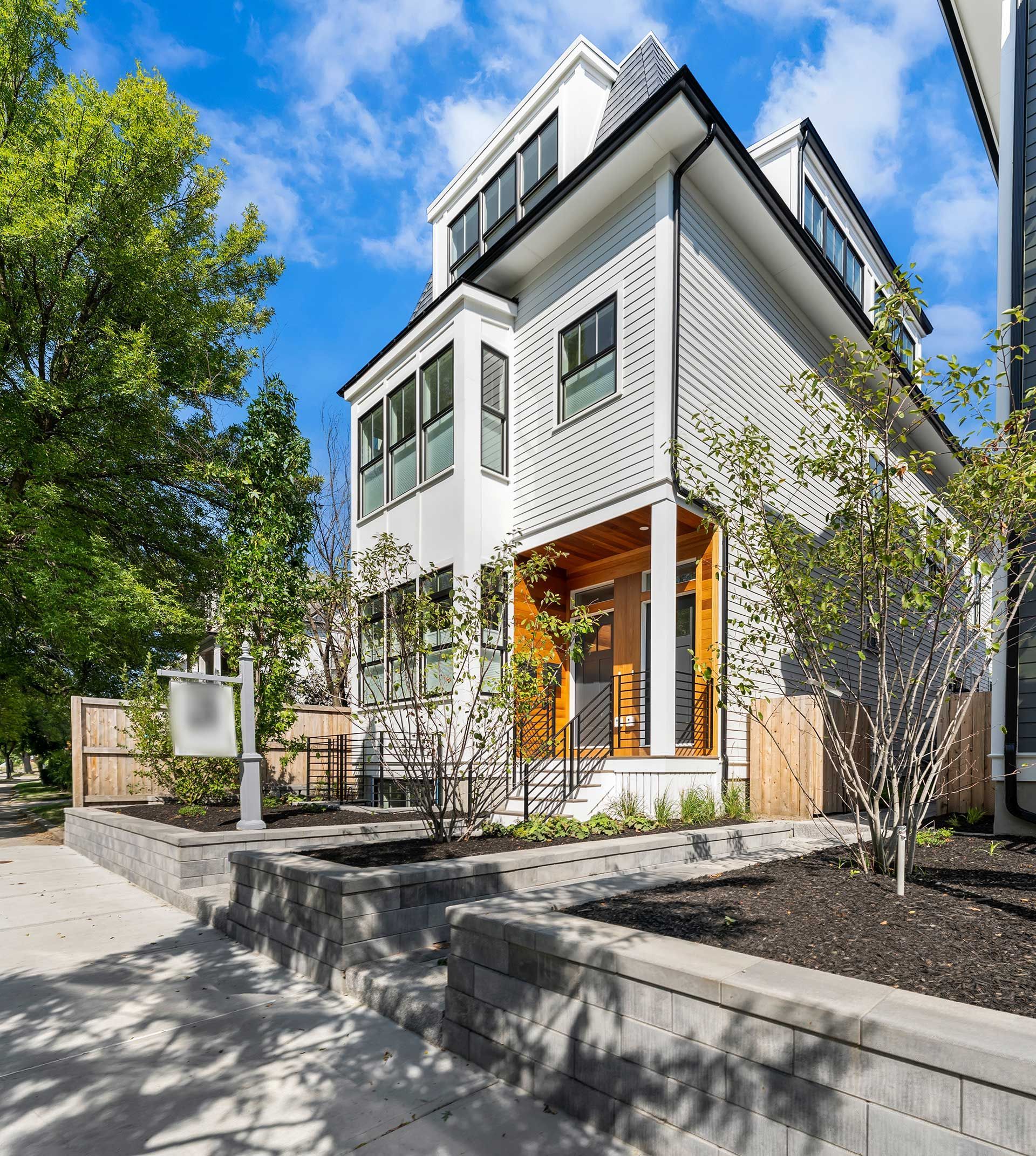 Modern white townhome with perforated facade, wooden accents, and a small front garden under a blue sky.