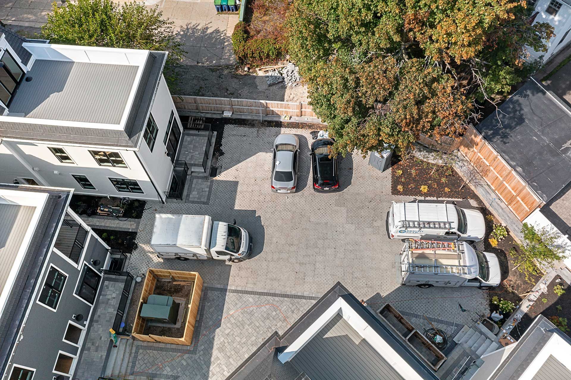 Aerial view of a parking lot with several parked vehicles surrounded by buildings with gray and white exteriors.