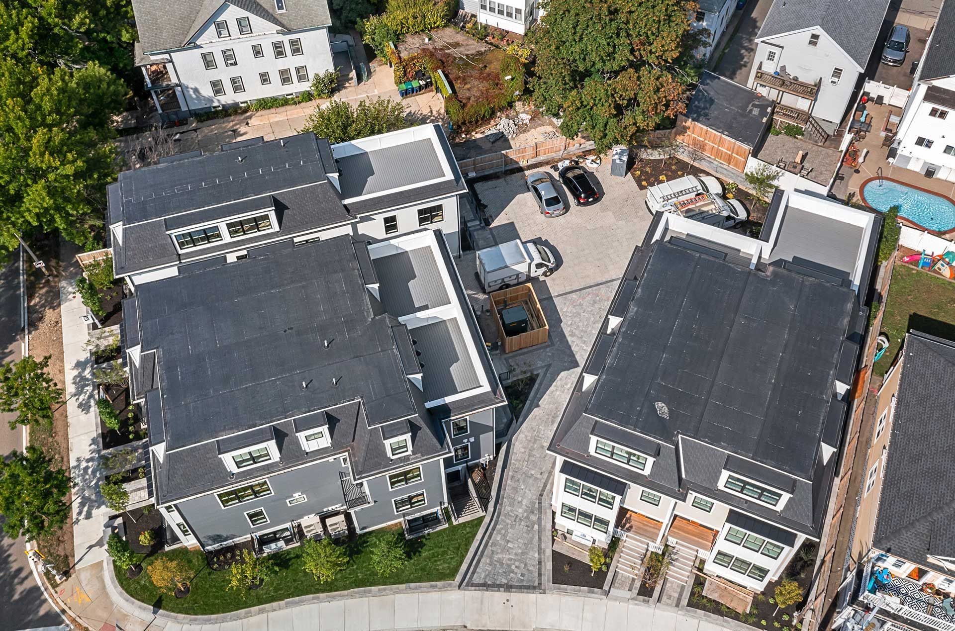 Aerial view of modern grey townhouses with black roofs and a small parking area.