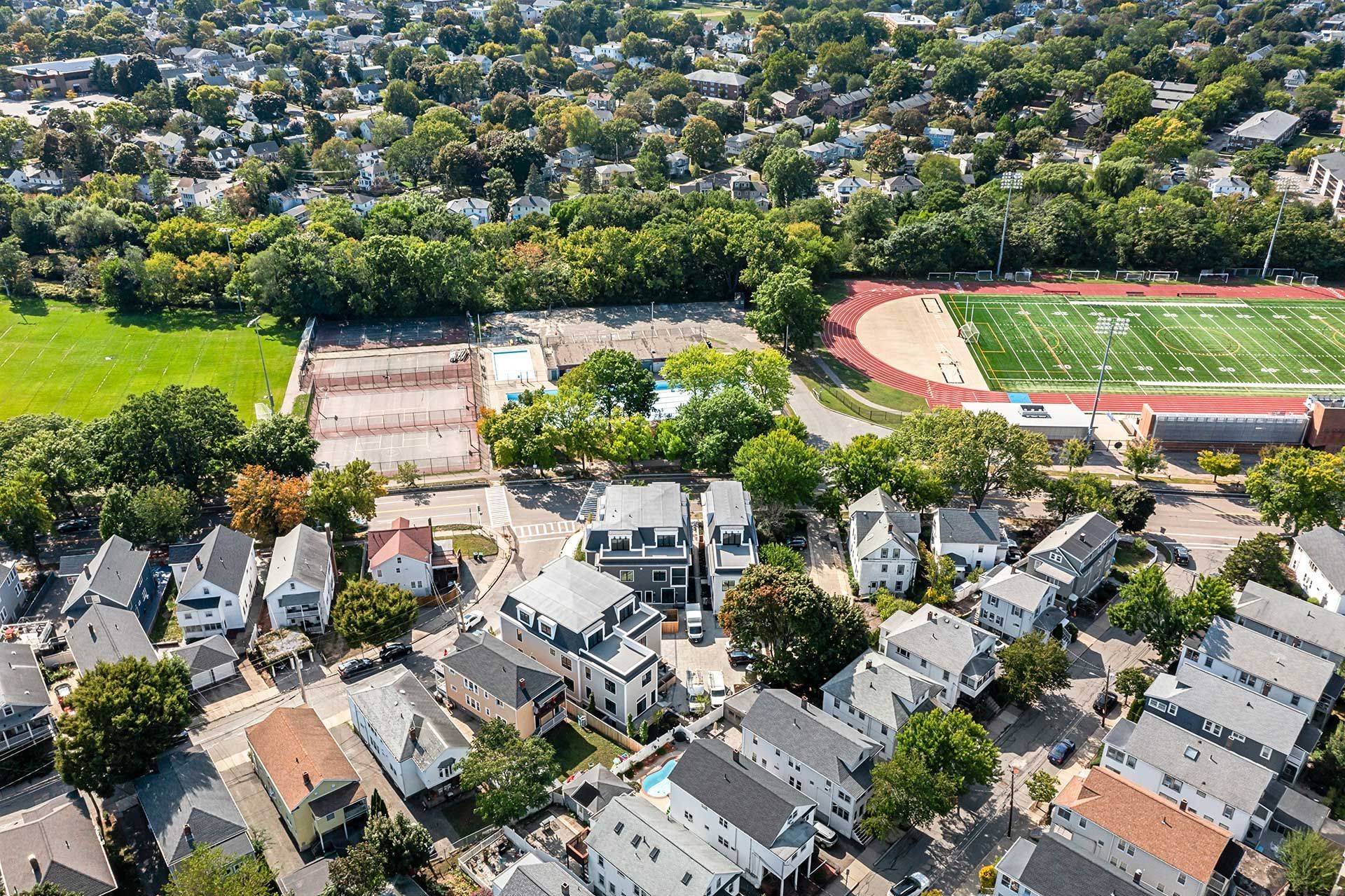 Aerial view: residential neighborhood next to a stadium and a park-like area with trees.