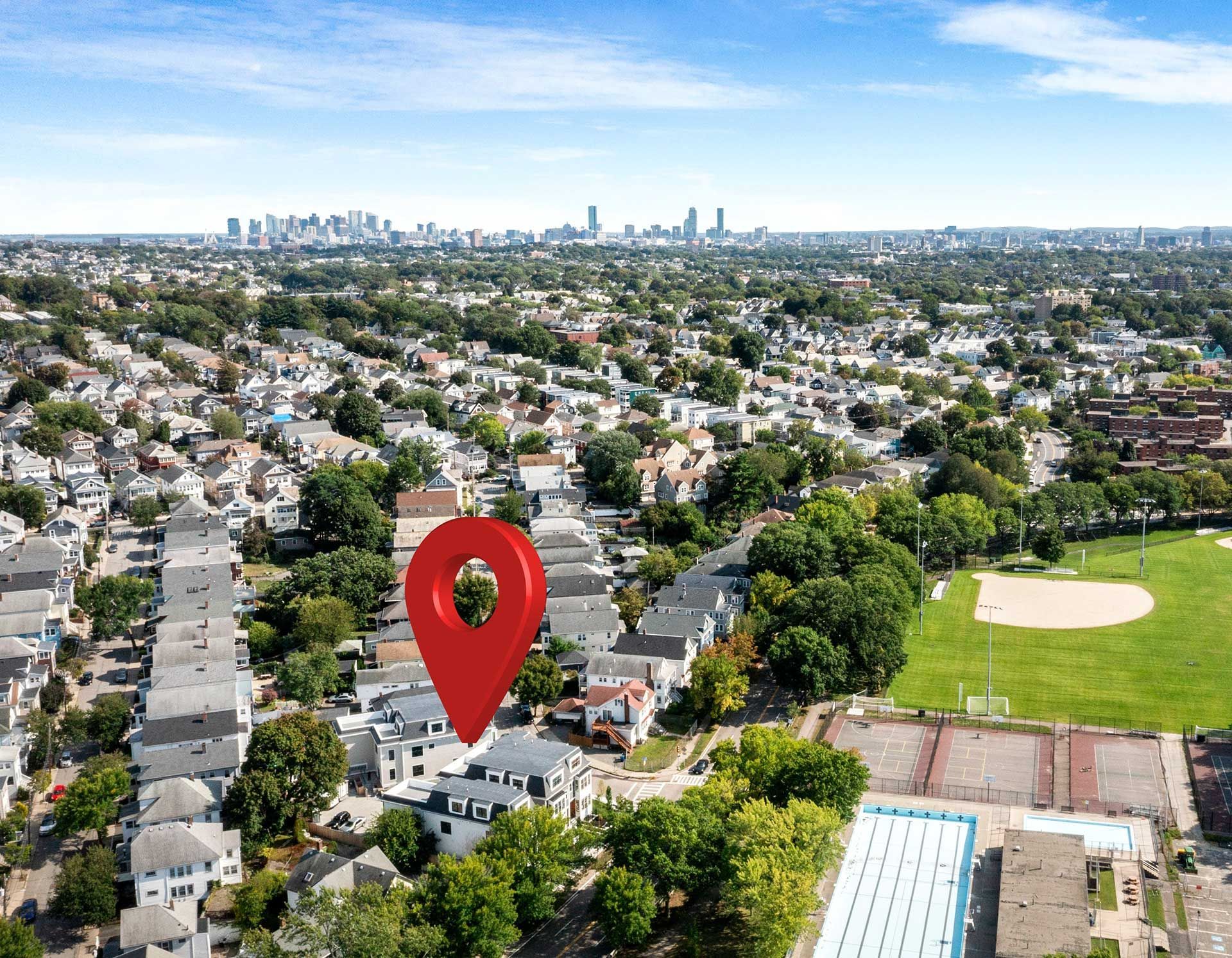 Aerial view of neighborhood with red location pin, city skyline in the background.