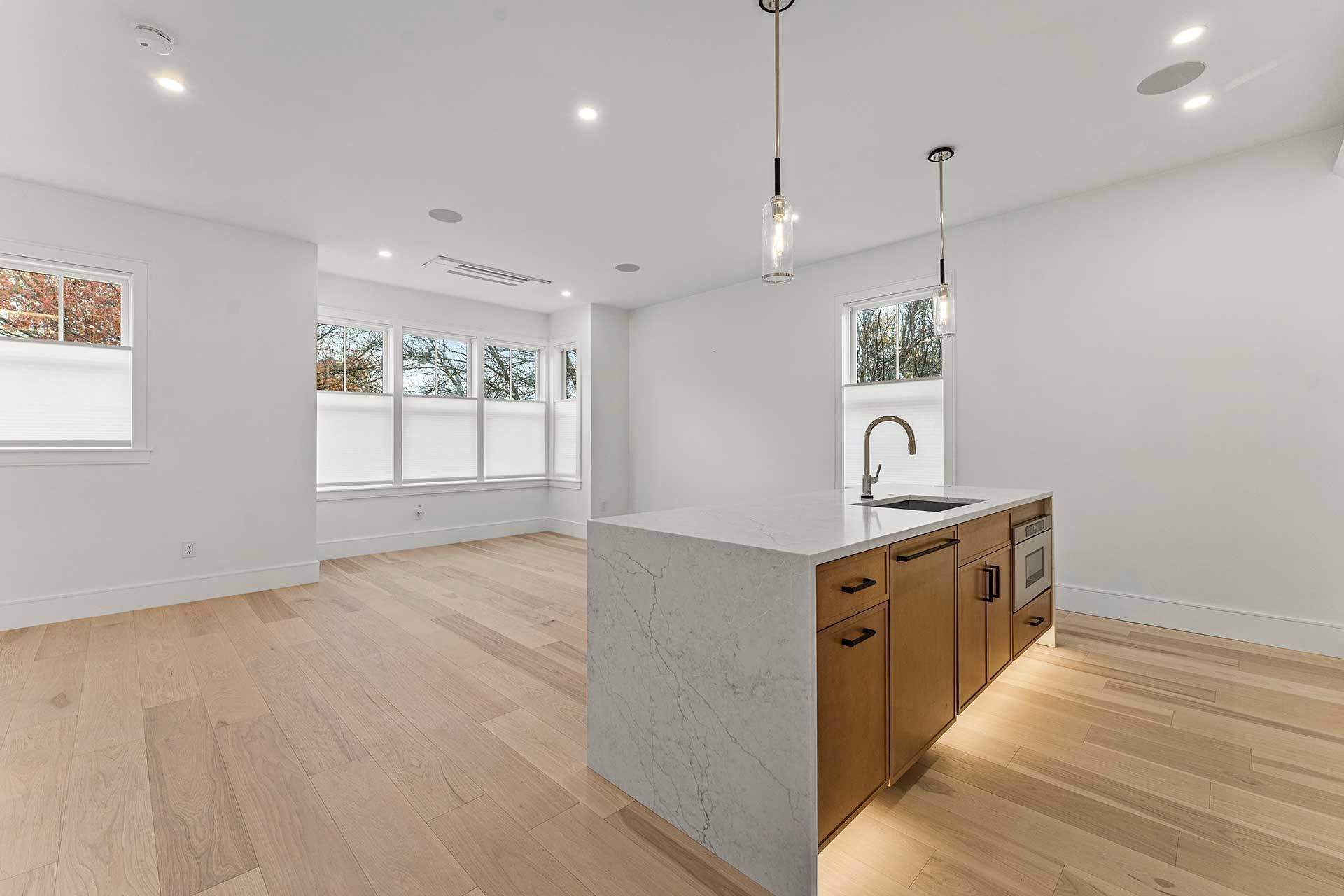 Modern kitchen with island, light wood floor, white walls, and pendant lights.