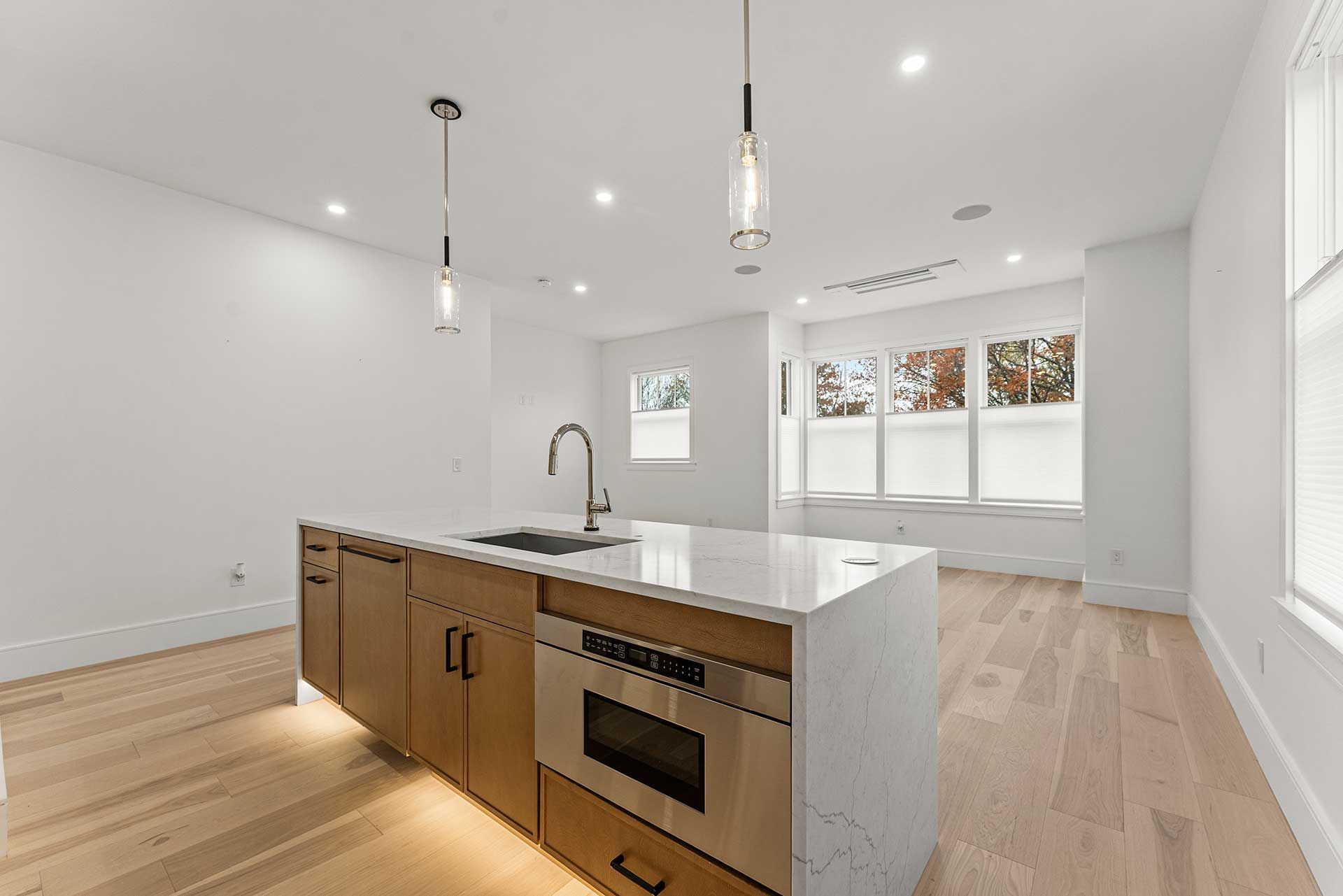 Modern kitchen with light wood floors, island with sink and microwave, pendant lights.