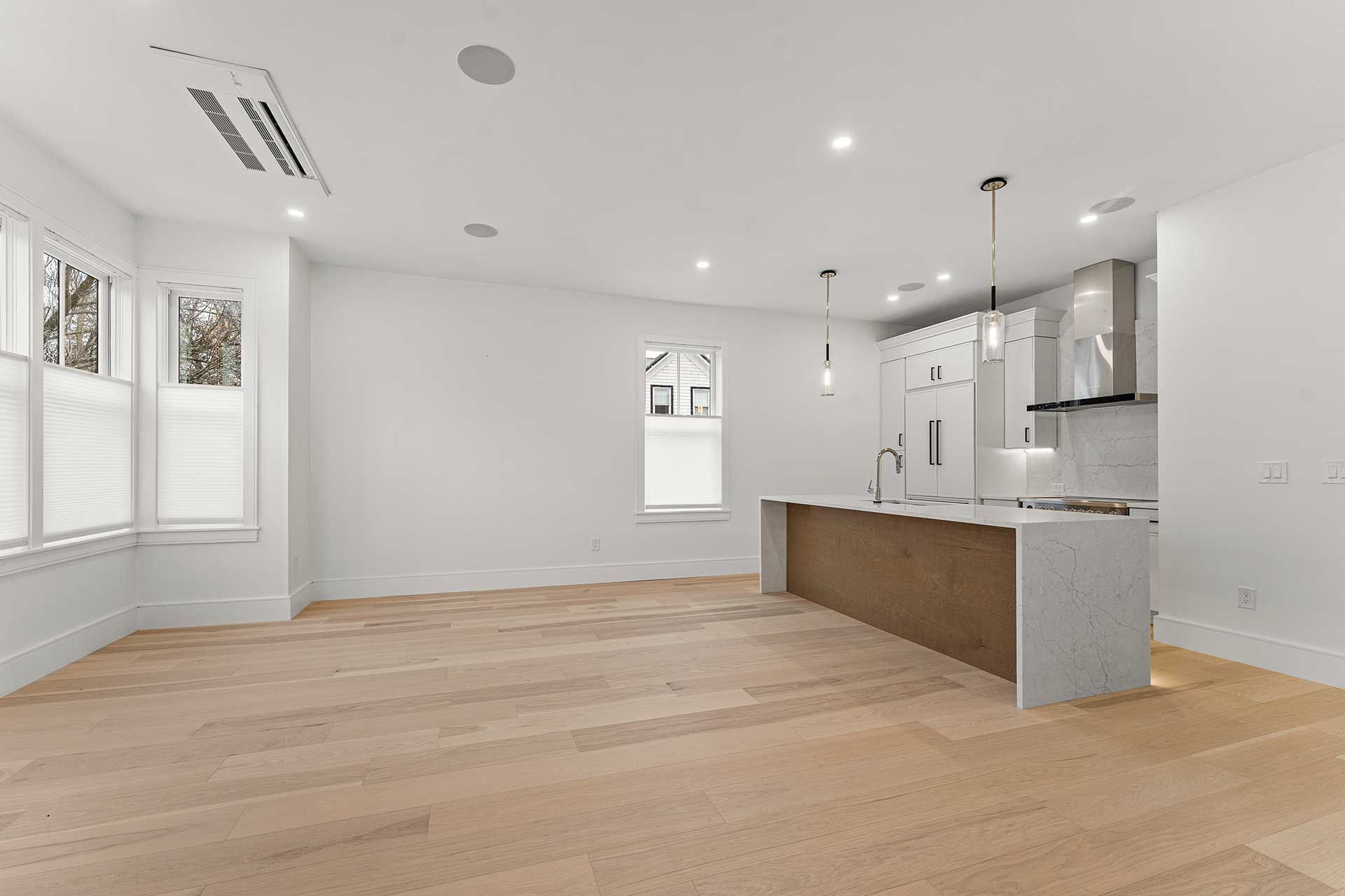 Spacious, empty living area with wood flooring, white walls, and a kitchen island.