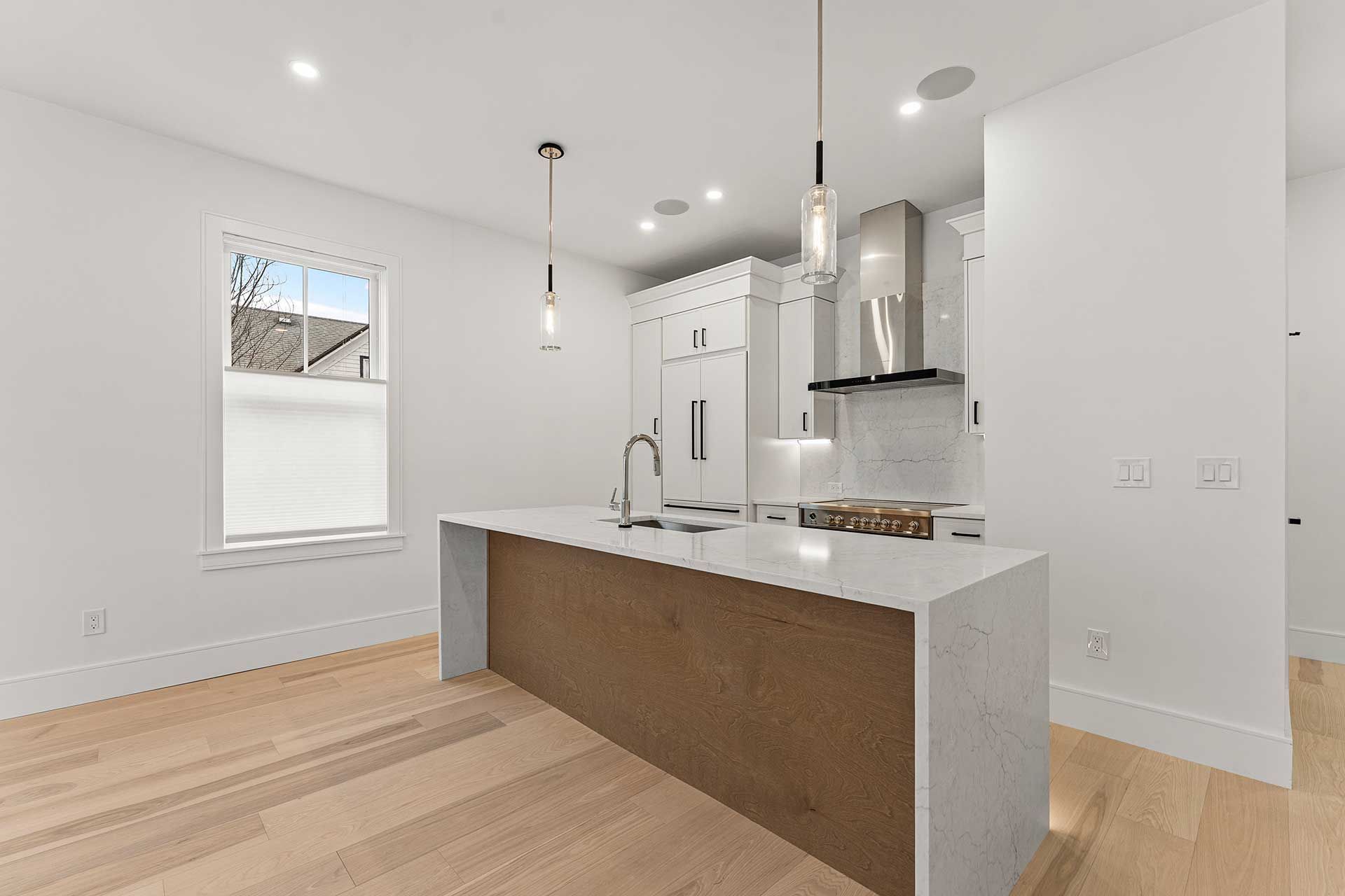 Modern kitchen with white countertops and cabinets, brown island, and wood flooring.