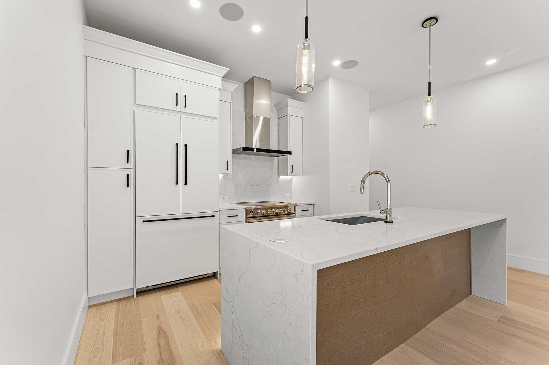 White kitchen with island, stainless steel appliances, and wooden floors.