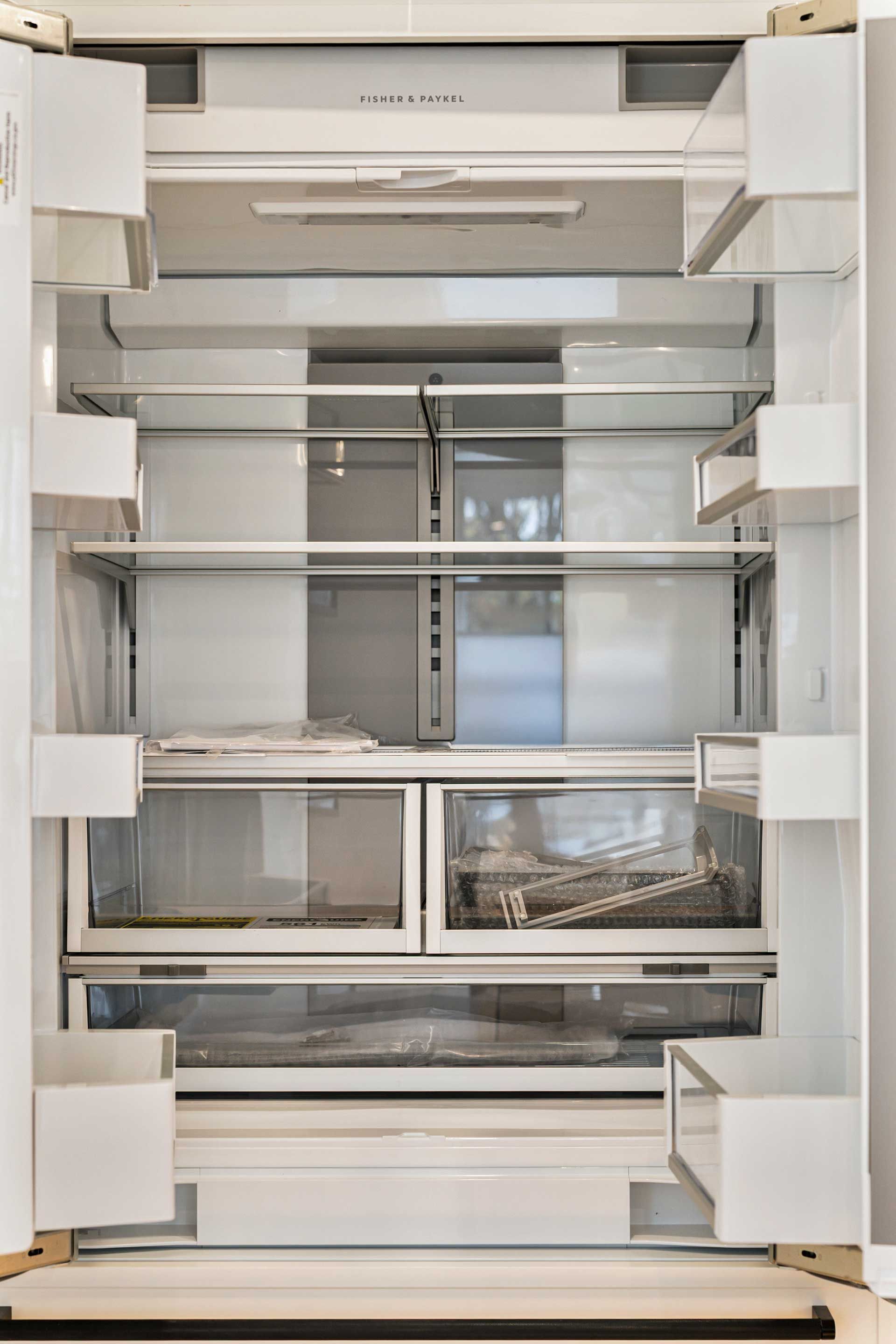 Empty, open refrigerator. White interior with shelves, drawers, and door compartments.