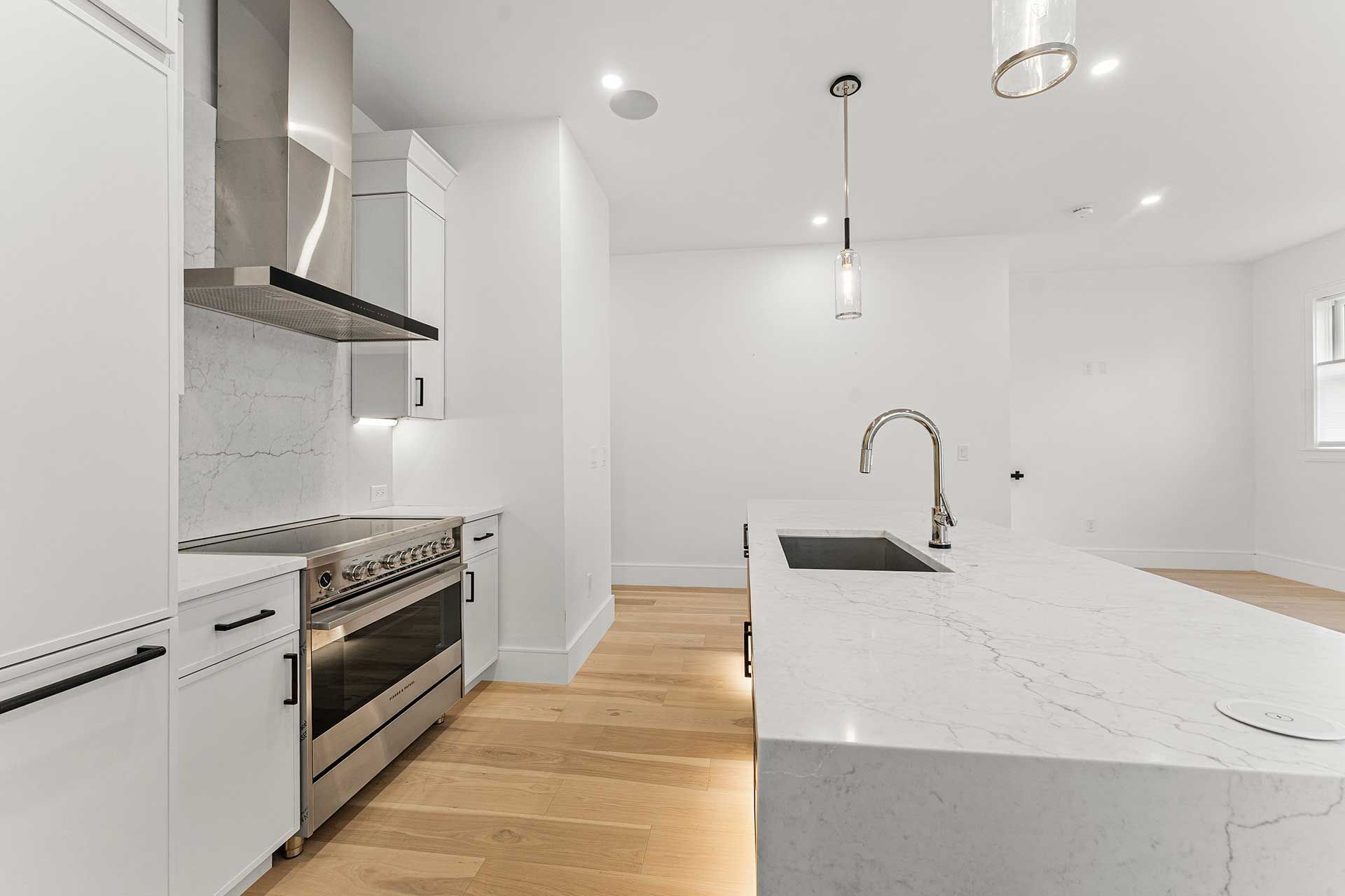 Modern white kitchen with stainless steel appliances, marble island, and pendant lighting.