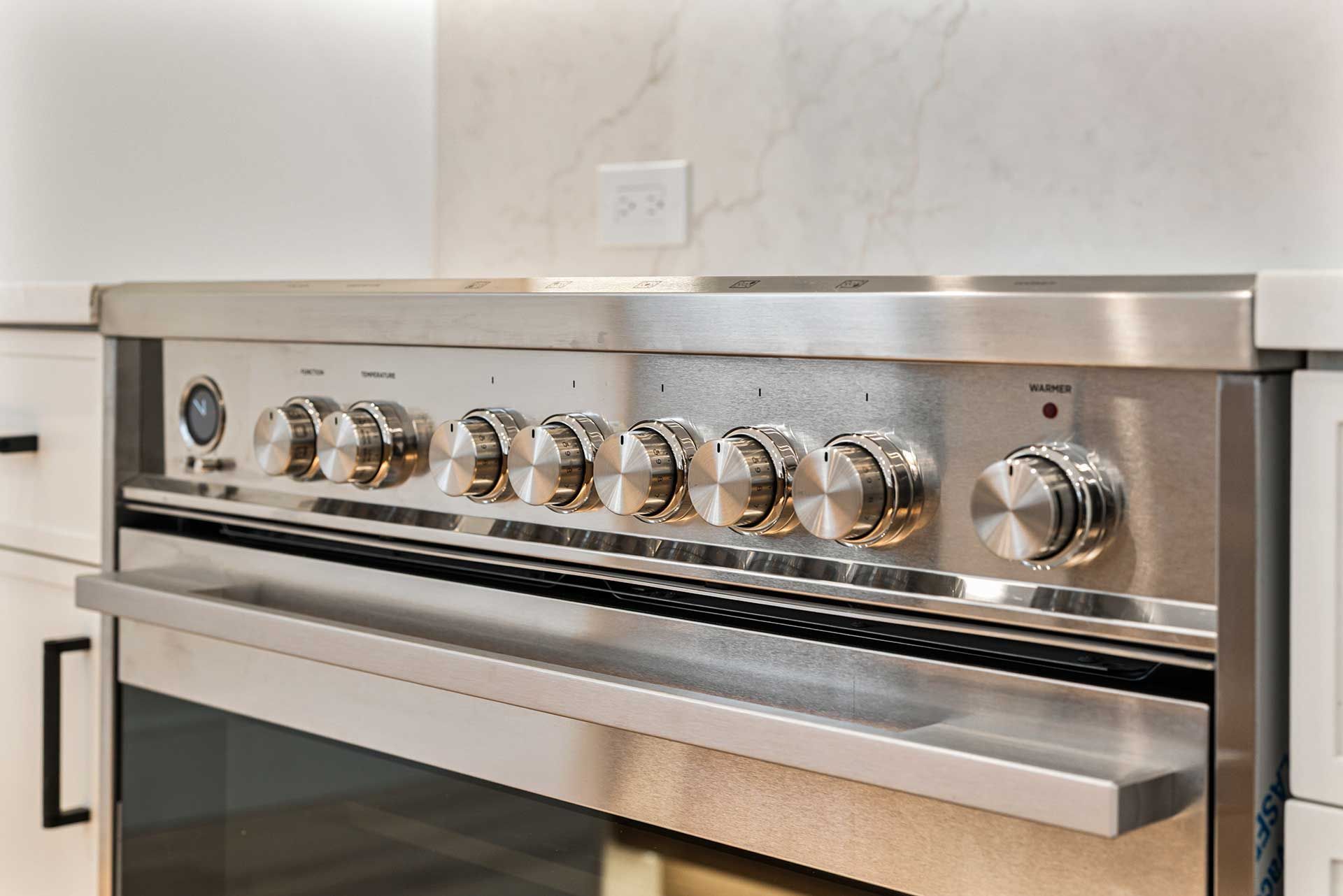 Stainless steel oven with multiple control knobs and a drawer, set in a kitchen.