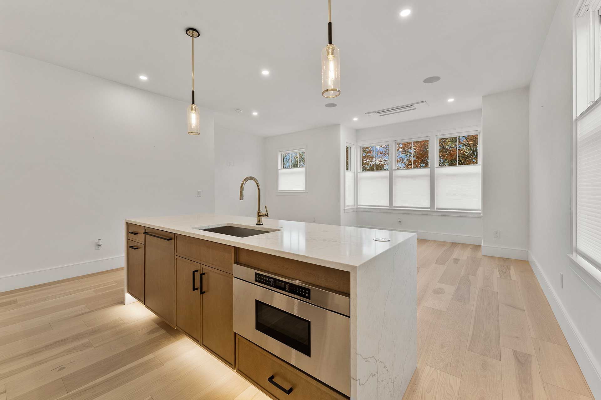 Modern kitchen with island, wooden cabinets, quartz countertop, pendant lights, and large windows.