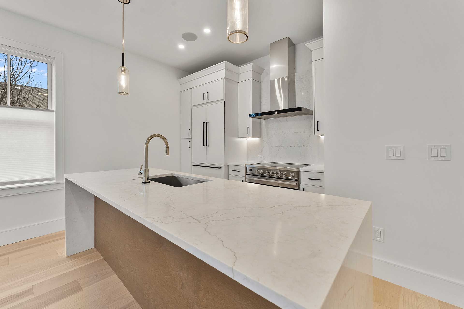 Modern white kitchen with island, sink, and stainless steel range hood.