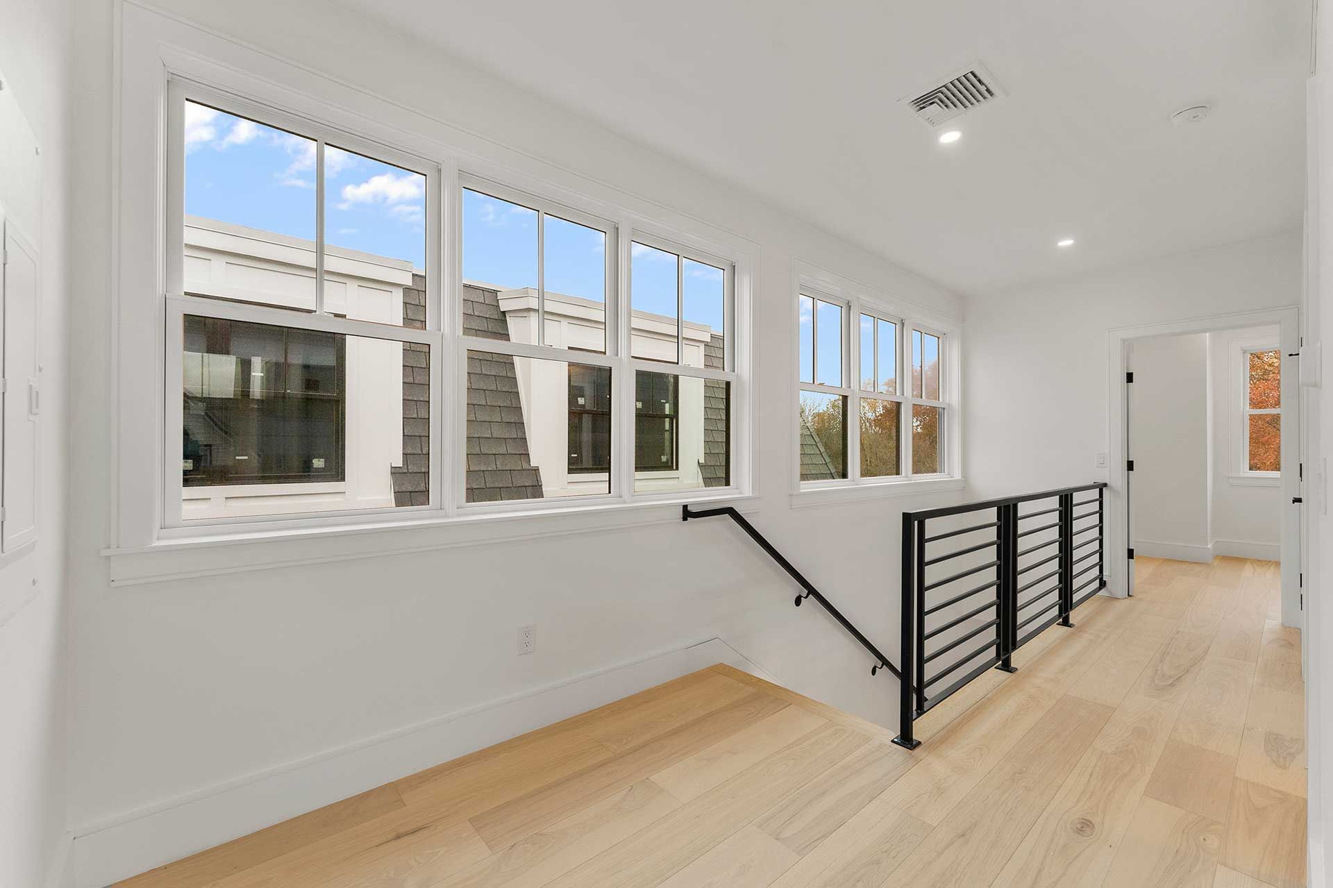 Hallway with windows, light wood floor, and black railing.