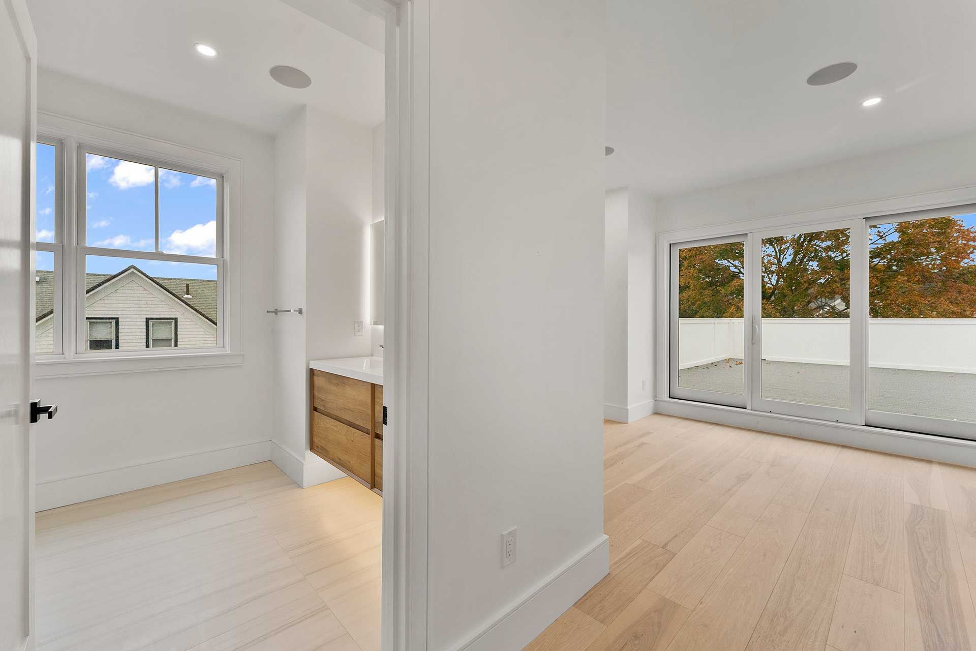 Bright modern room with wood floors and white walls; bathroom on the left, balcony doors on the right.