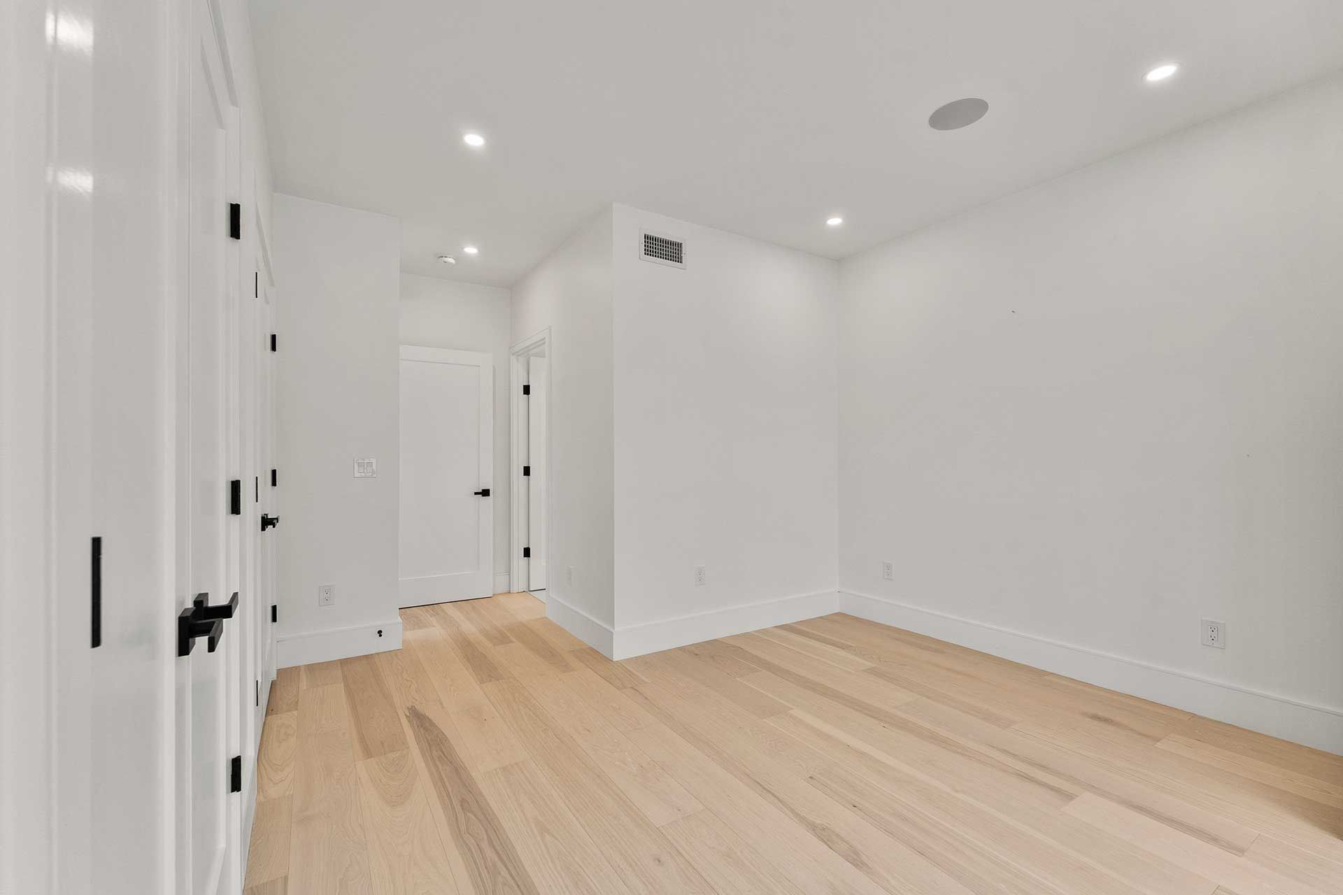 Empty room with white walls, light wood floors, and black door hardware.