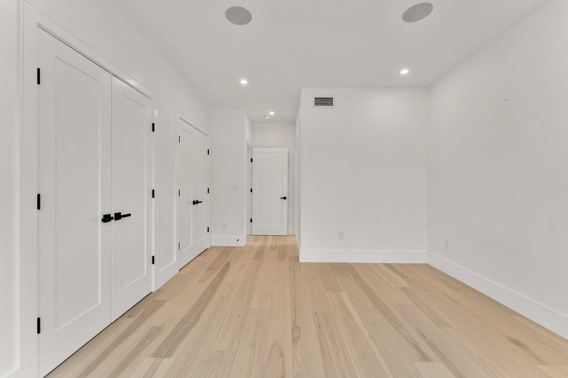 Empty room with light wood floors, white walls, and closed white doors.