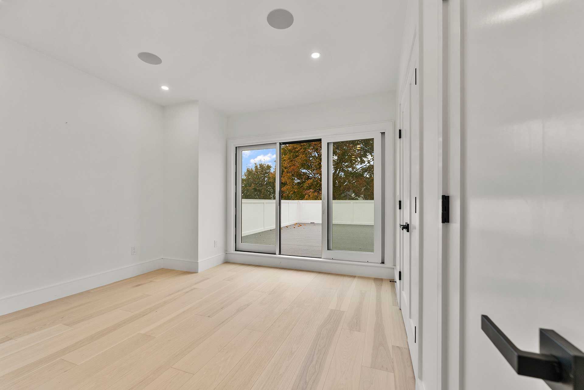 Empty room with light wood floors, white walls, and sliding glass door to exterior.