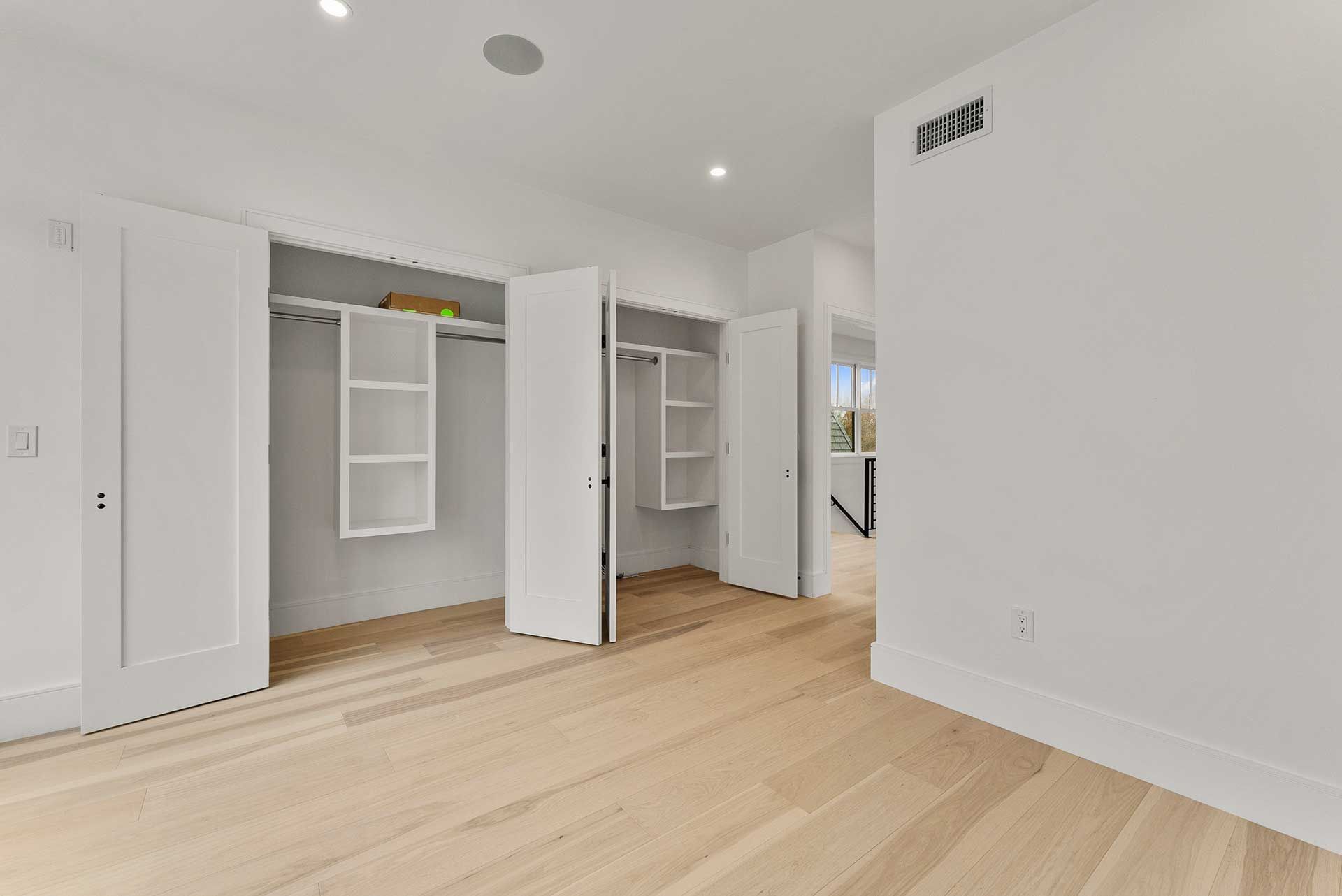Empty bright room with wood floors, closets, and white walls.