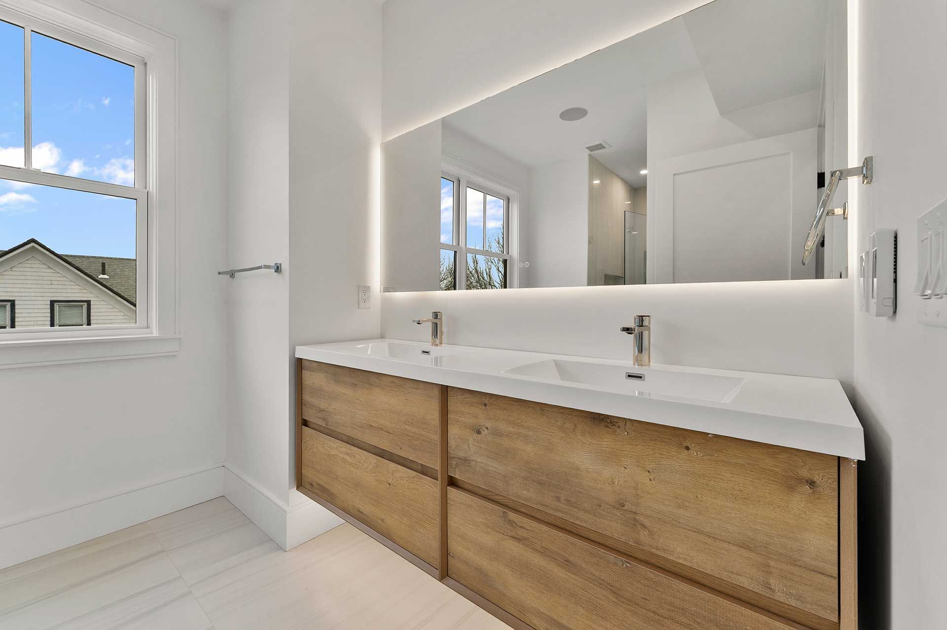 Modern bathroom with double vanity, large mirror, and window.