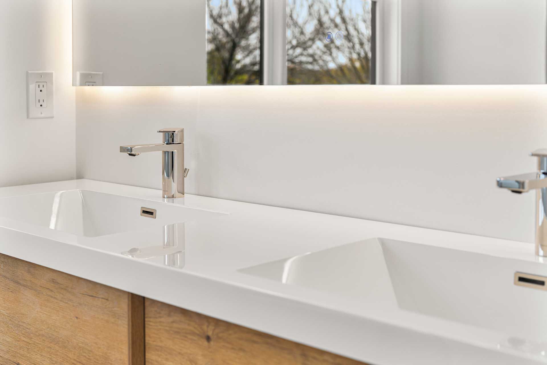 White double sink with chrome faucets and a backlit mirror.